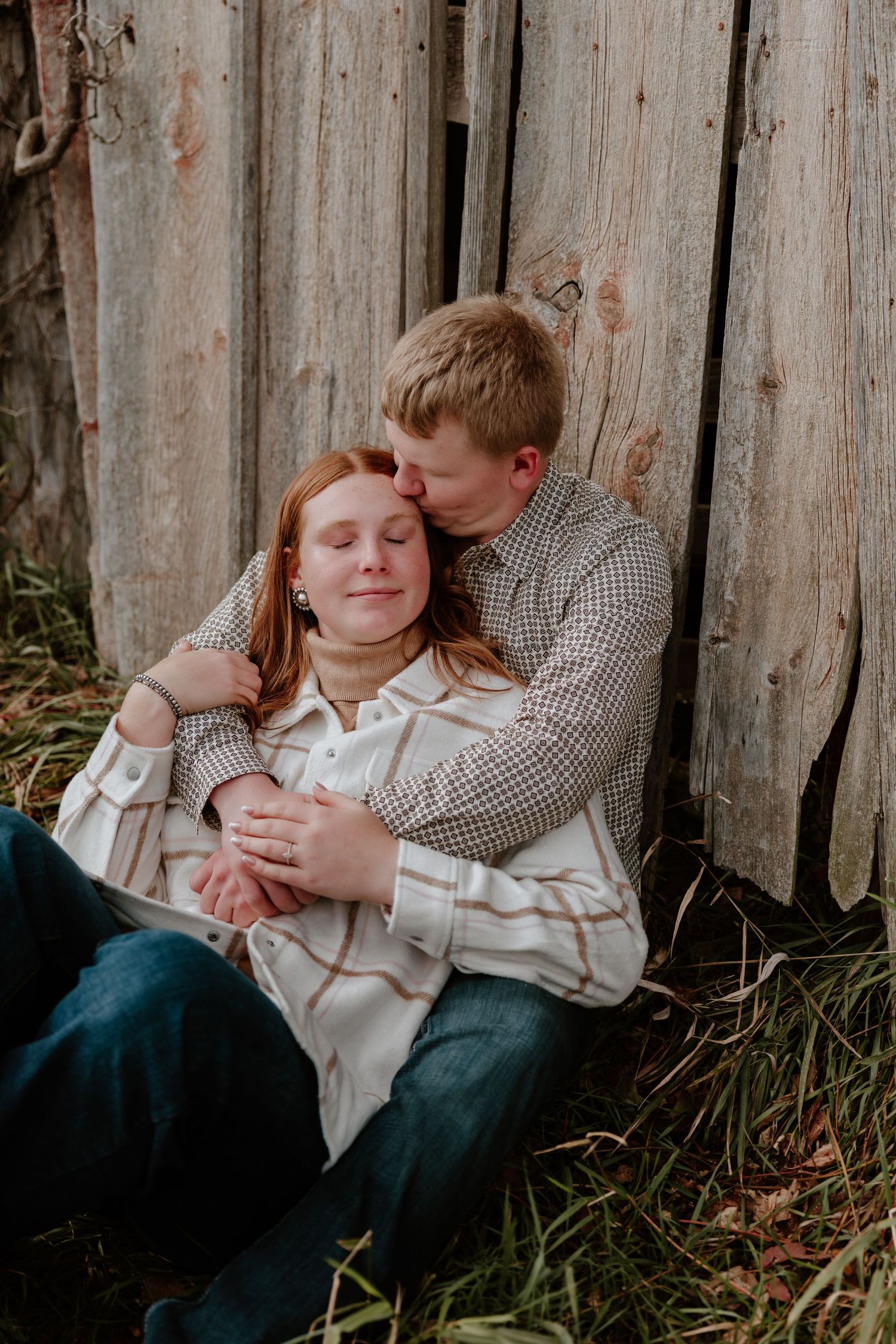Romantic couple in casual attire sharing tender moments against a rustic wooden fence background.