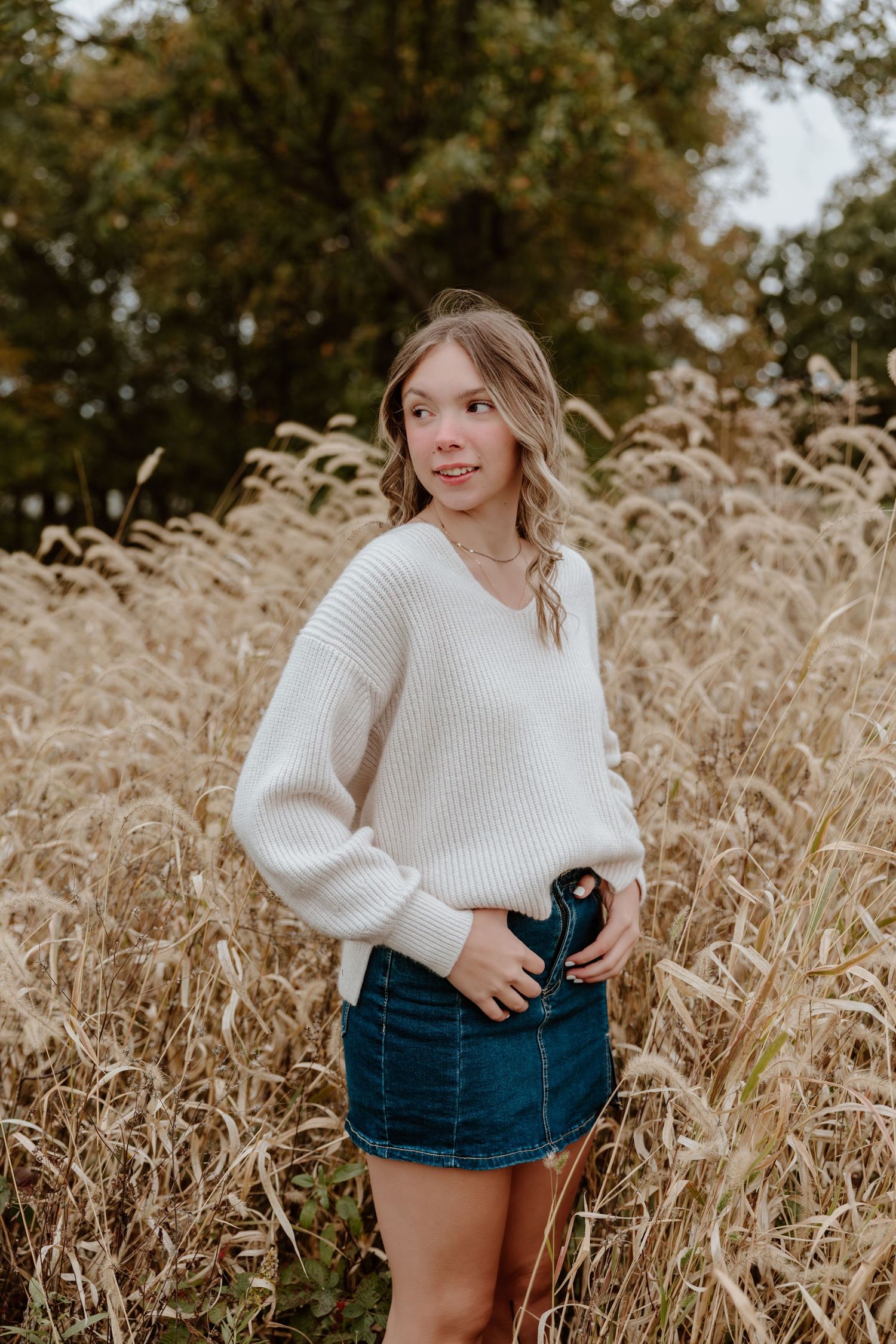 Woman in white sweater and denim shorts poses in golden wheat field during autumn photoshoot.