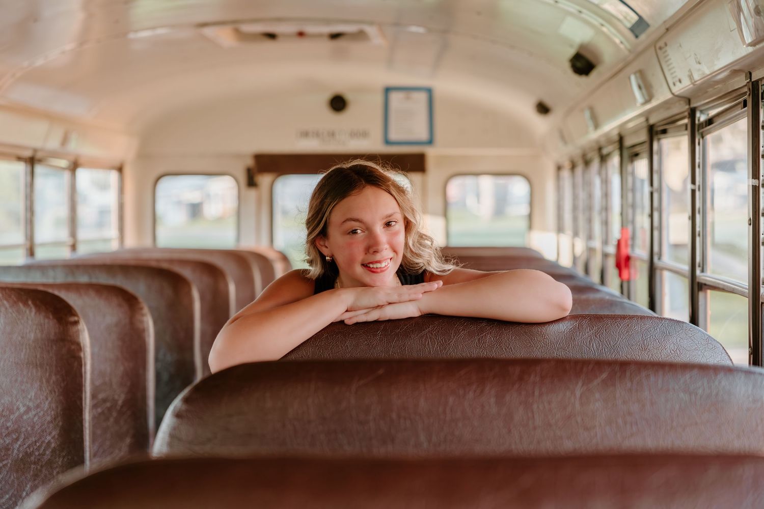 Student rests on brown leather bus seat inside vintage yellow school bus interior during golden hour.