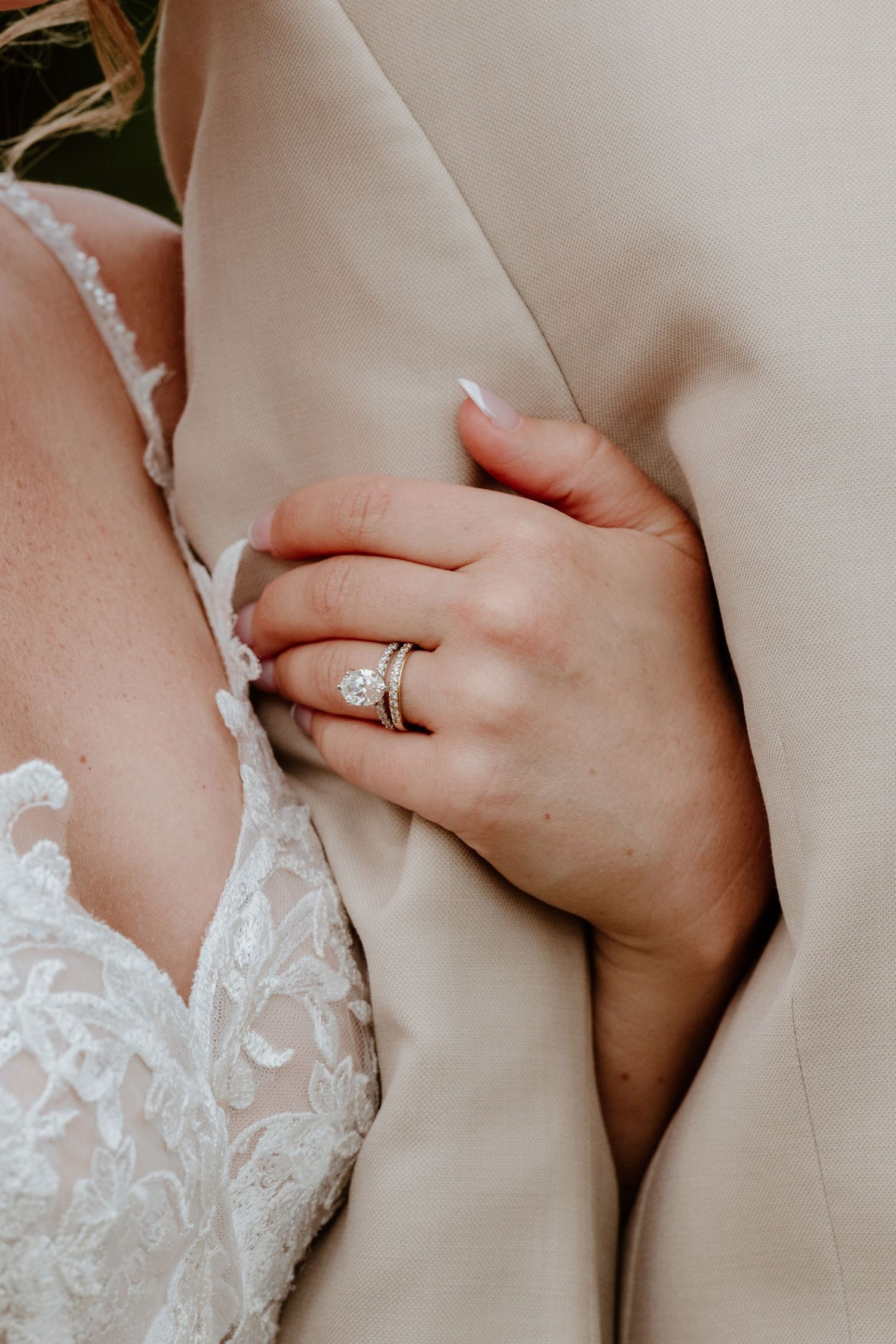 Close-up of bride's hand showing diamond engagement ring and wedding band while holding groom's suit lapel.