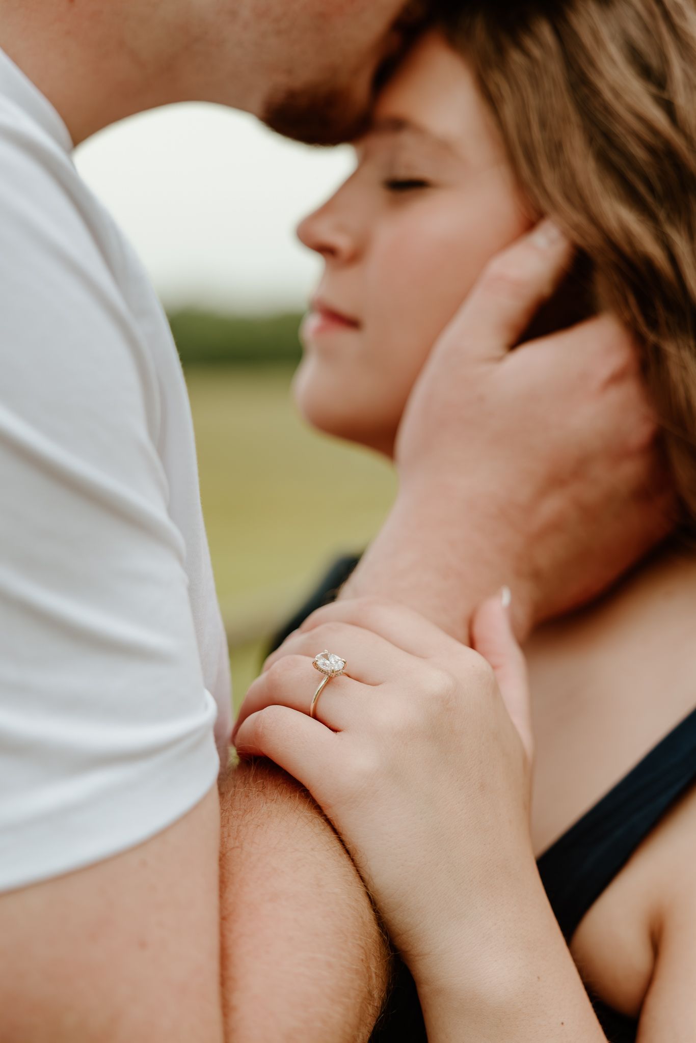 Couple sharing an intimate moment outdoors, woman wearing a diamond engagement ring on her hand.