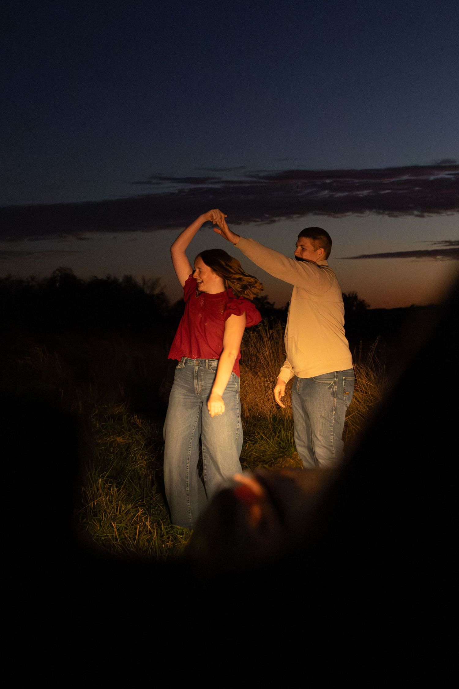 A sequence of silhouettes against a dark evening sky shows people dancing and moving in a field at twilight.