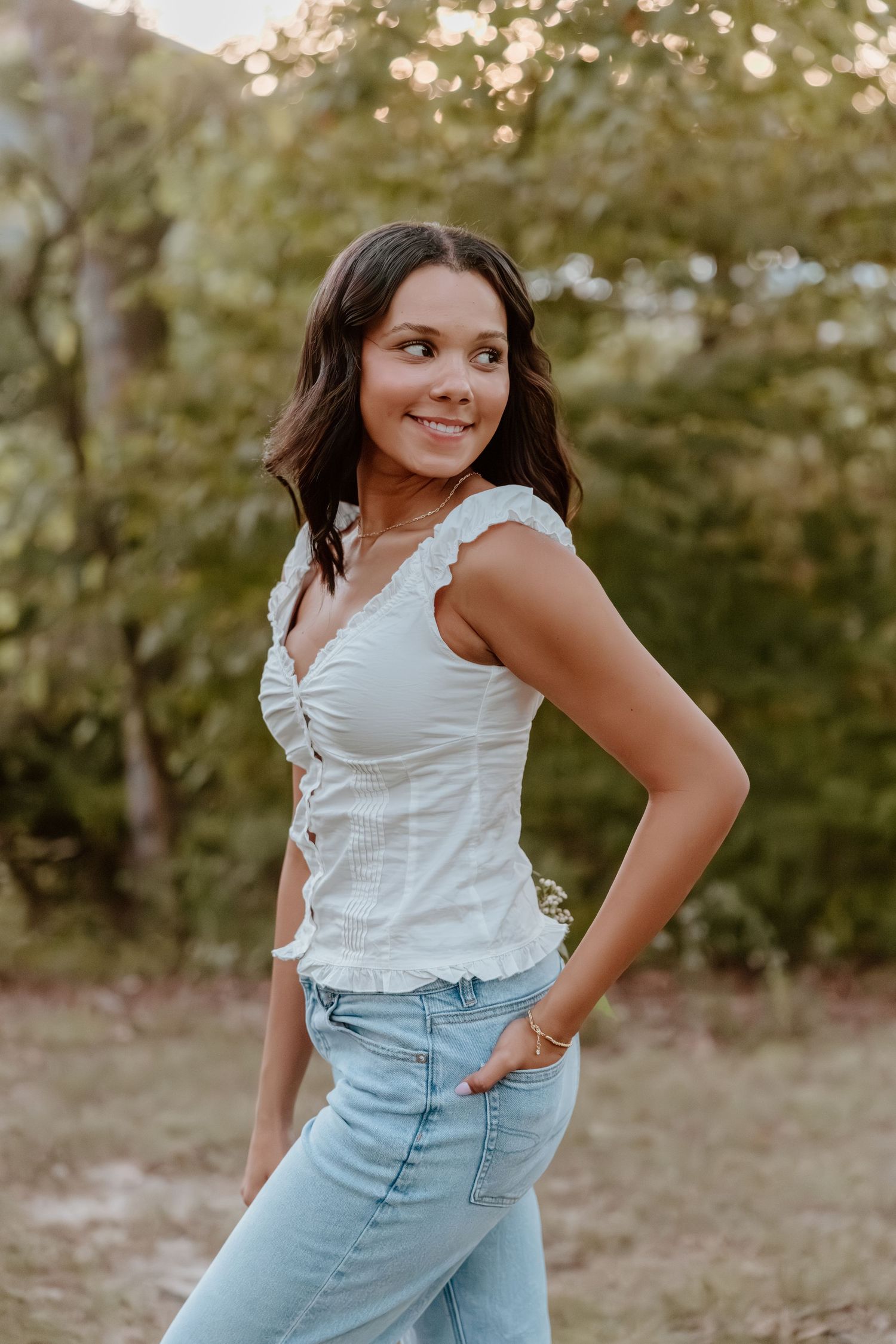 A casual outdoor photoshoot featuring someone in a white top and light blue jeans against a natural background.