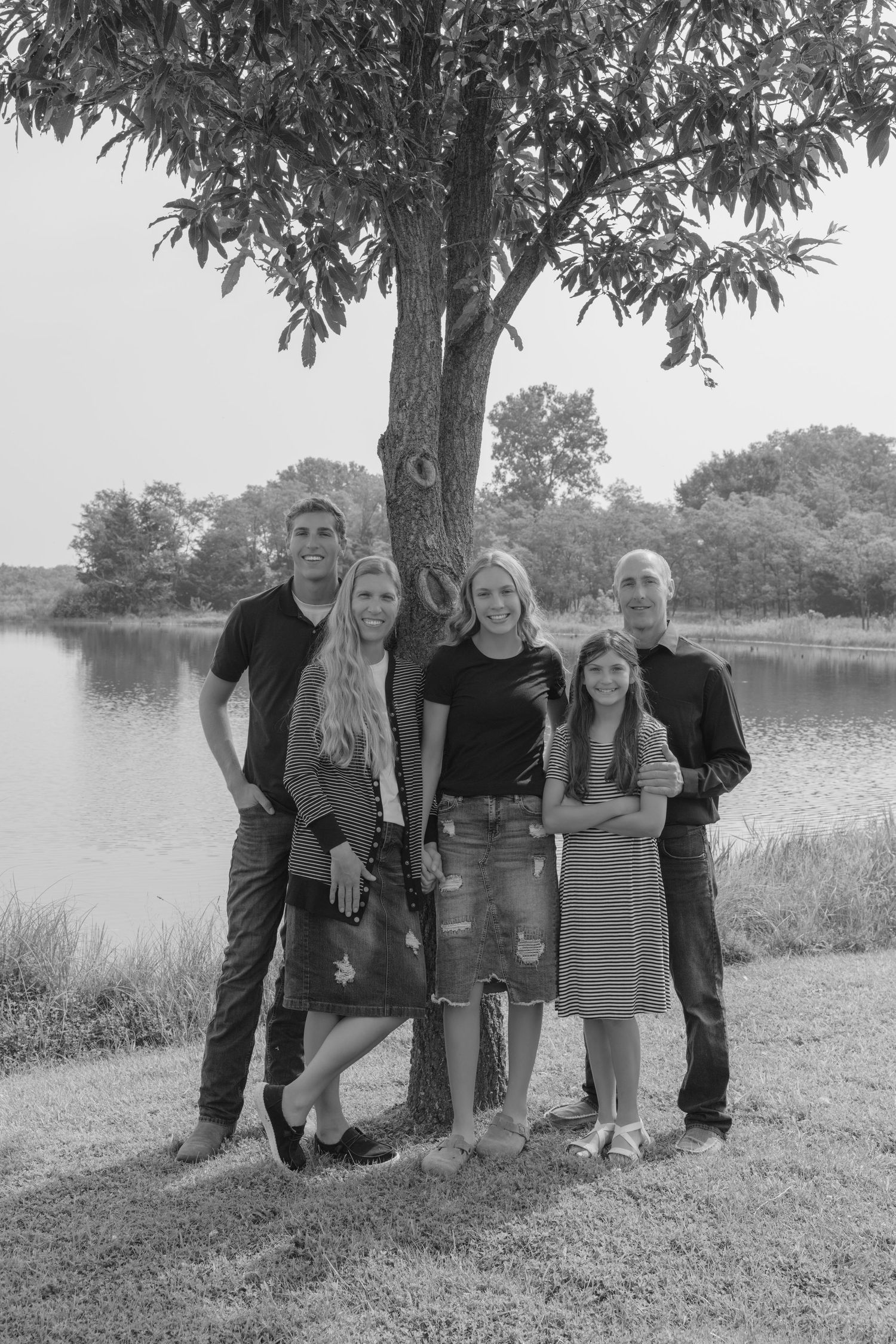 Black and white photo of a group standing together under a tree by a lake on a sunny day.