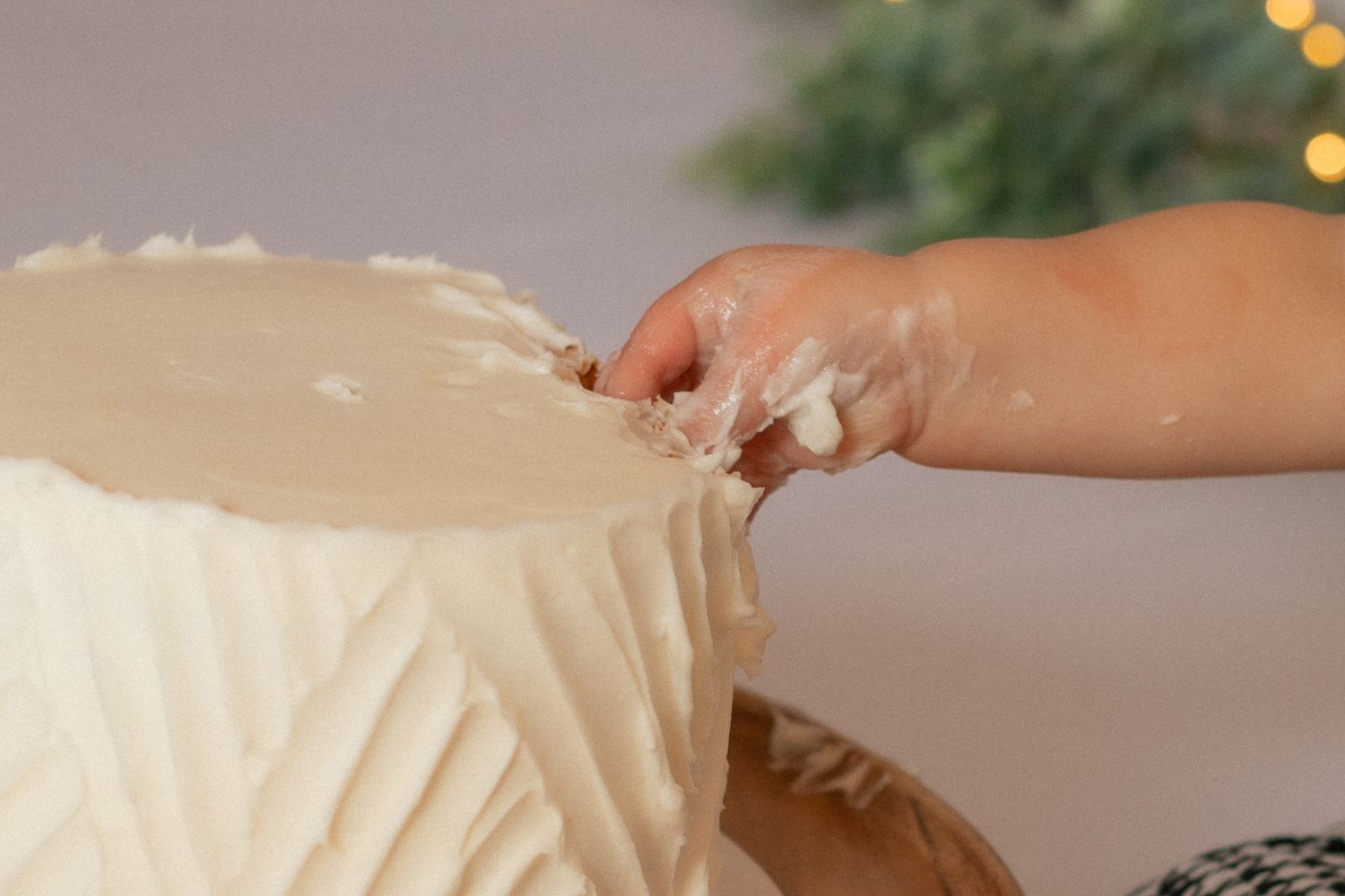 Close-up of small hands touching the frosting on a white cake.