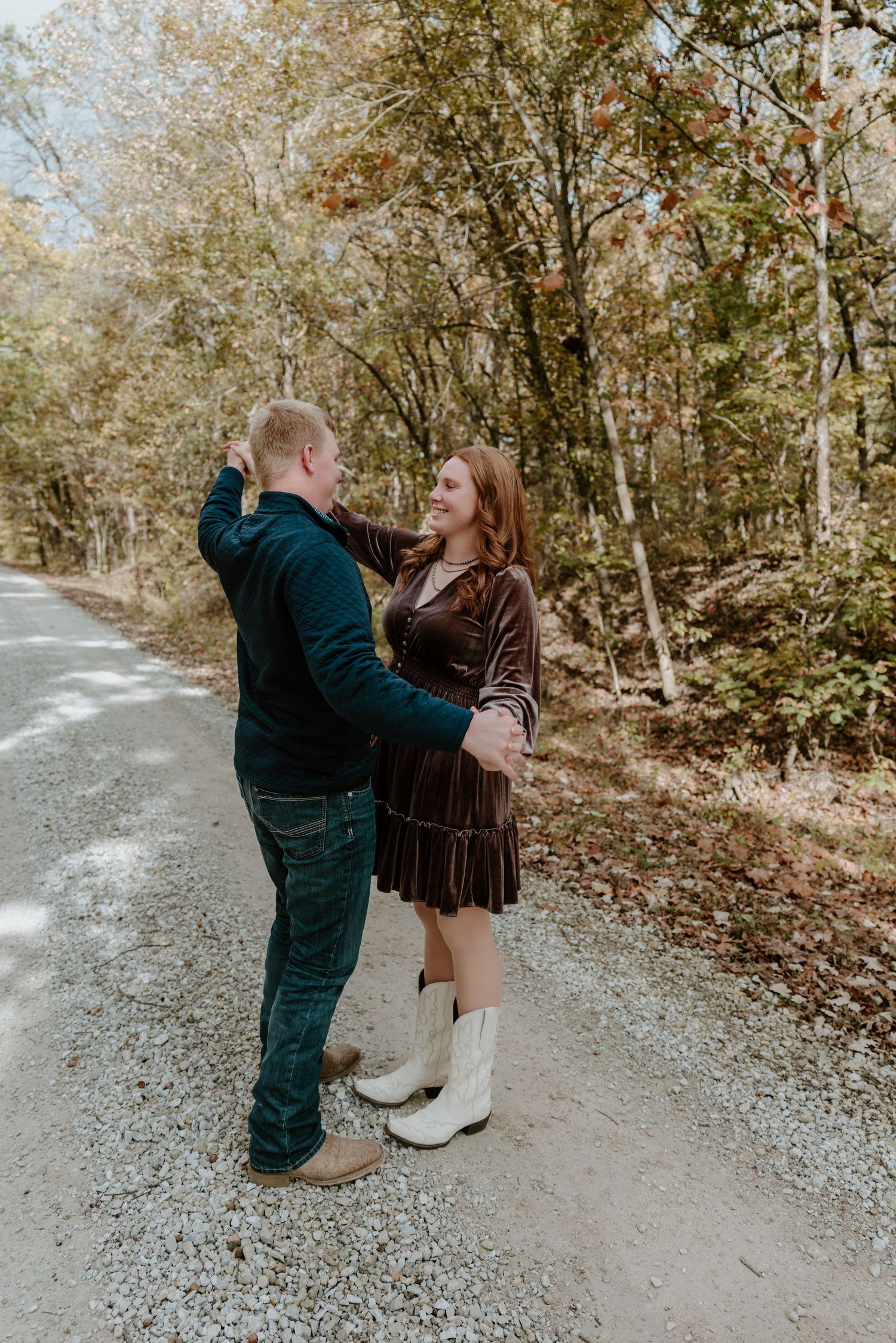 A couple shares playful moments together on a wooded path during an autumn photoshoot.