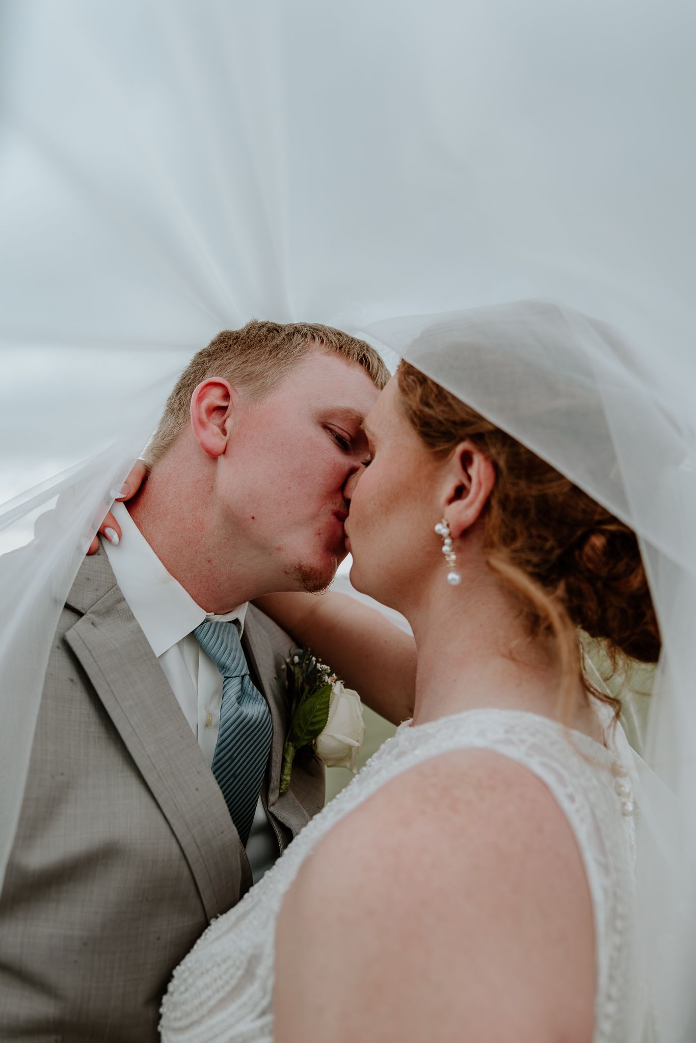 Newlyweds share a romantic kiss under a flowing white veil on their wedding day.