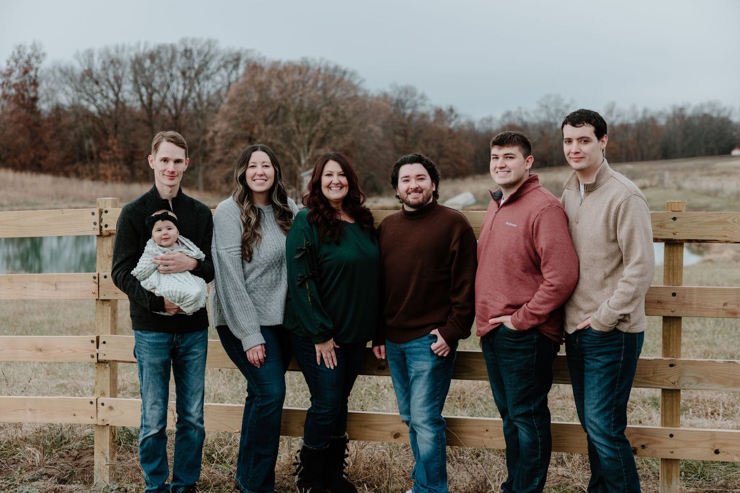 A group poses together outdoors against a rustic wooden fence on an autumn day.