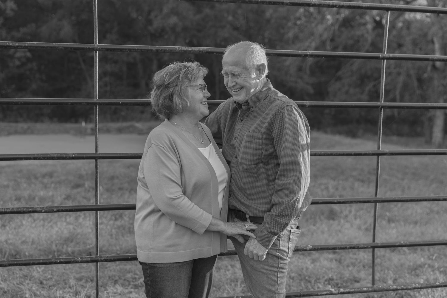Couple in casual attire shares a tender moment while standing by a metal fence in an outdoor setting.
