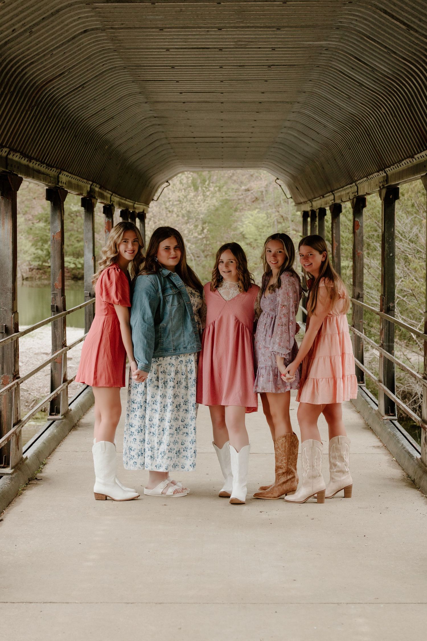 A group in vintage-inspired dresses and white boots pose together in a covered walkway with arched ceiling.