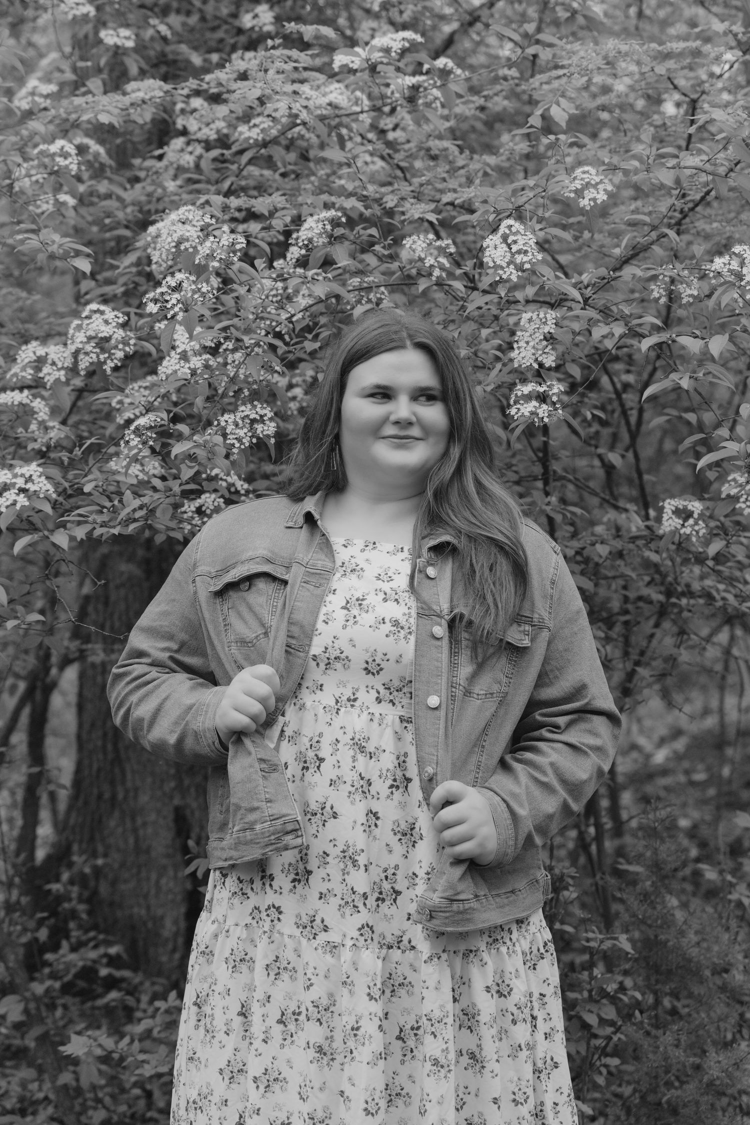 A series of black and white photos showing someone in a floral dress and denim jacket posing outdoors among trees.