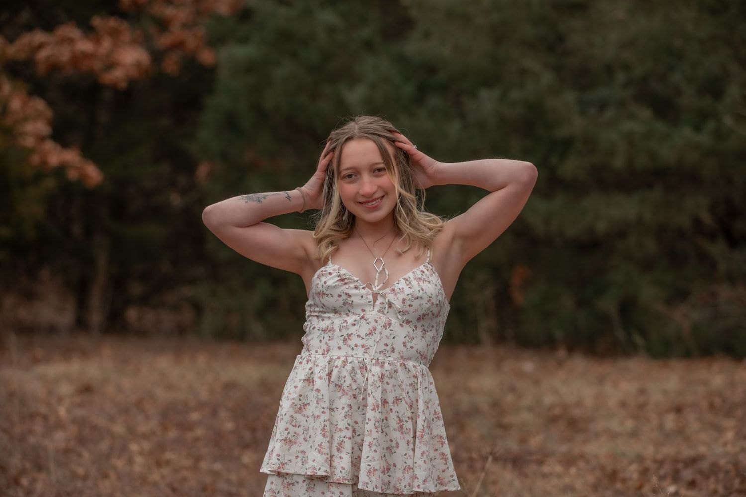 Portrait of someone in floral dress outdoors with hands in hair at sunset.