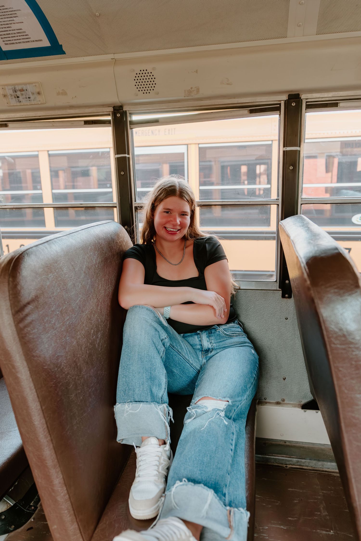 Student lounges across brown leather seats inside a sunlit school bus.