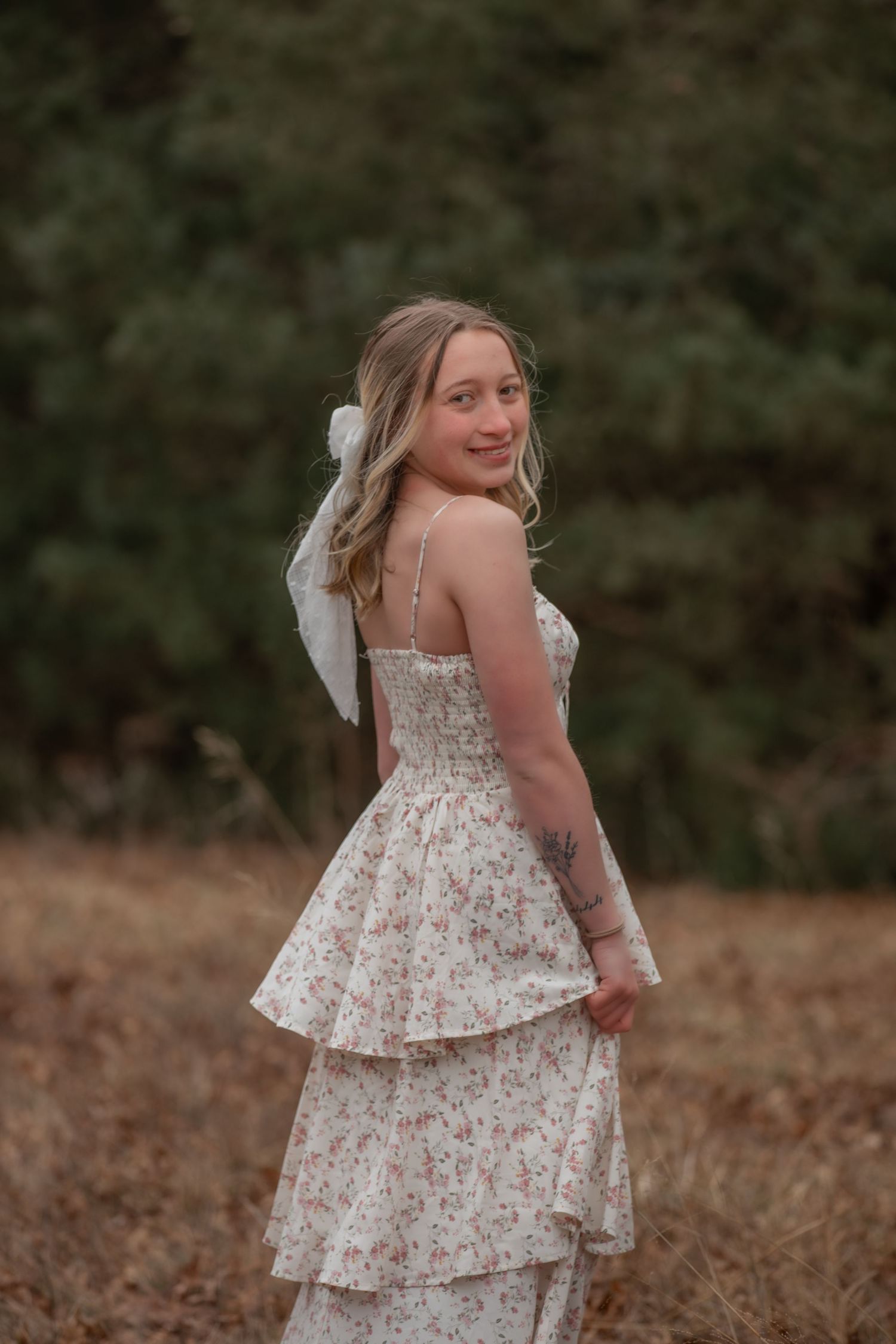 A person in a floral tiered dress poses outdoors in a field during golden hour.