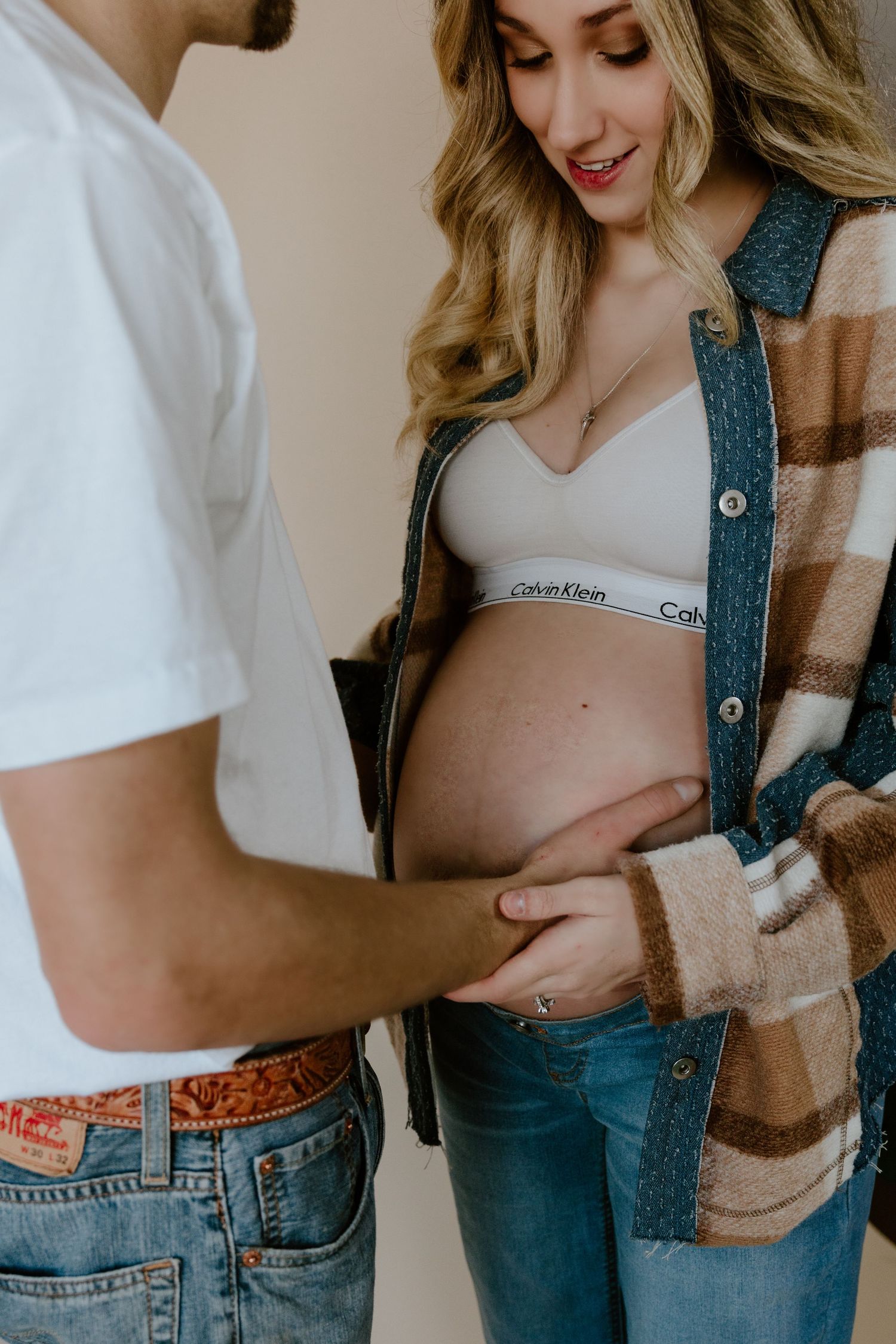 An intimate moment between an expectant couple as they lovingly touch the pregnant belly, wearing casual denim and sweaters.