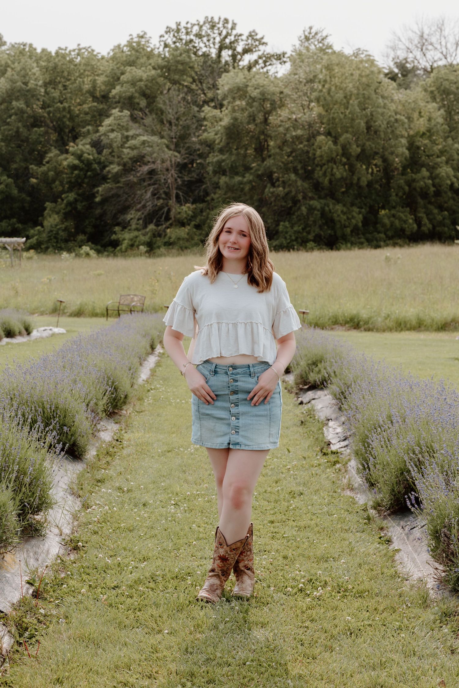 A person walks through a lavender field on a sunny day in denim shorts and boots.