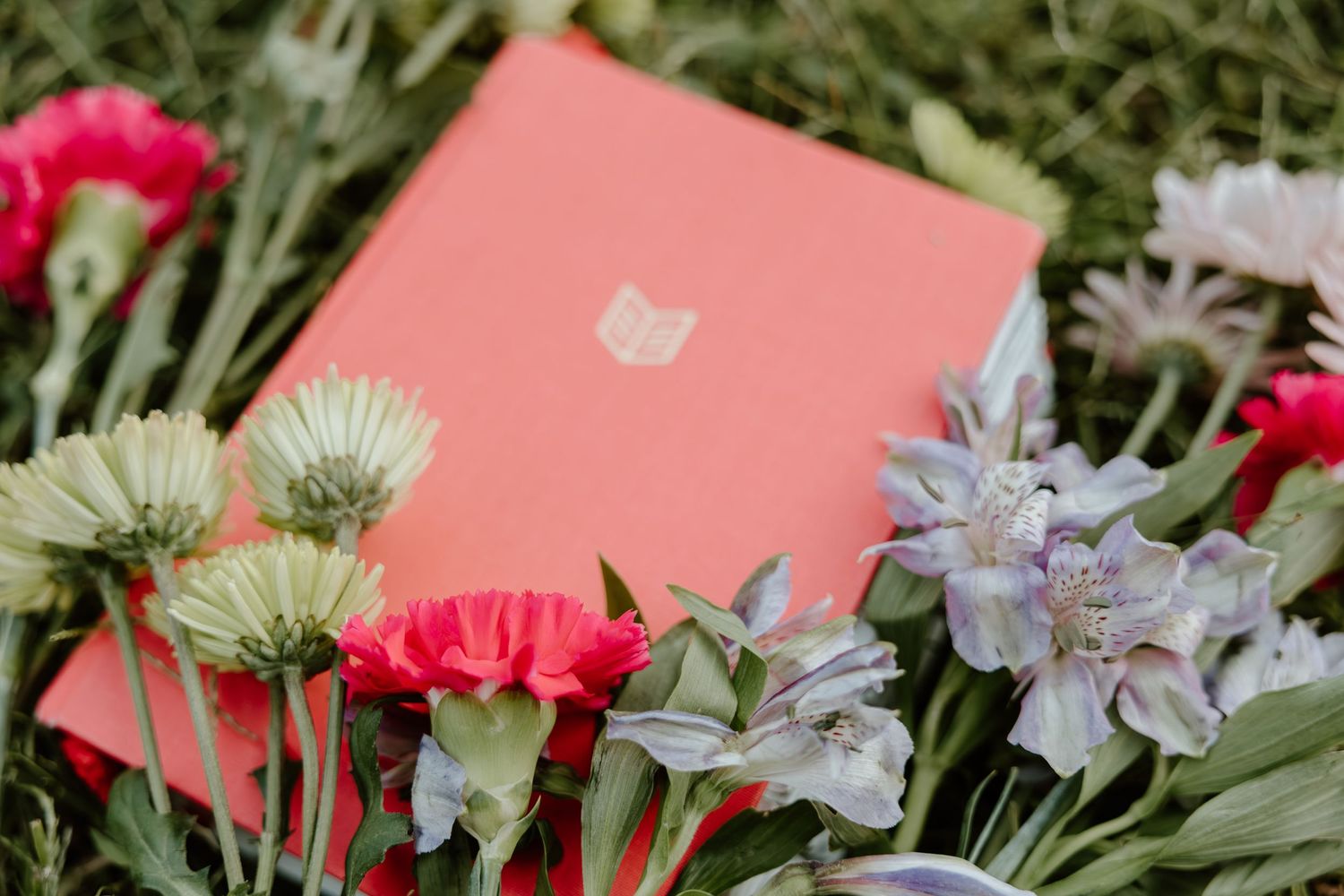 Colorful flowers and pink cards arranged on grass creating a spring-themed flat lay composition.
