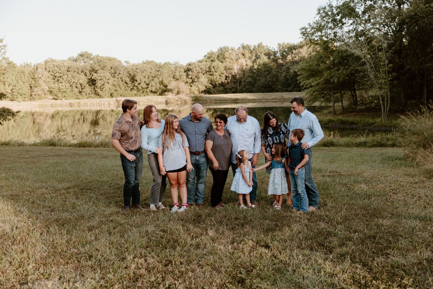 A group of people sitting and standing together in a sunny meadow during a casual outdoor photo session.