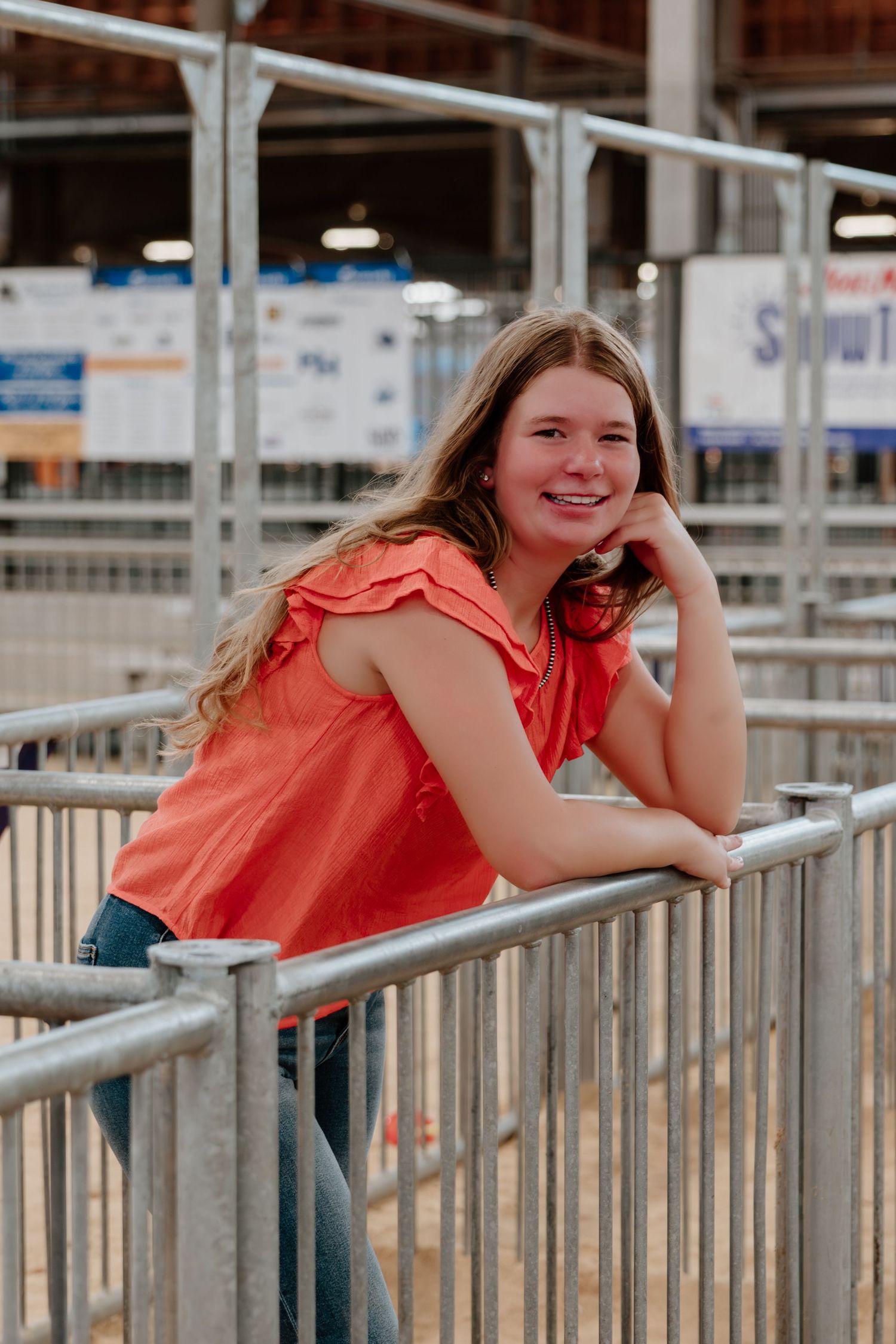 A figure in a coral-colored sleeveless top leans against metal railings at an outdoor venue during golden hour.