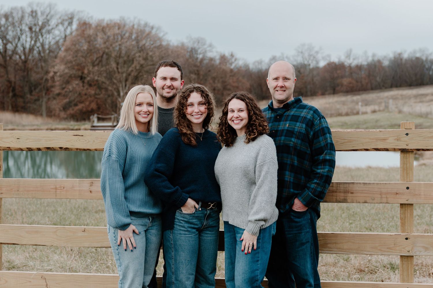 A group poses together outdoors near a wooden fence on a sunny winter day in coordinating blue and neutral outfits.