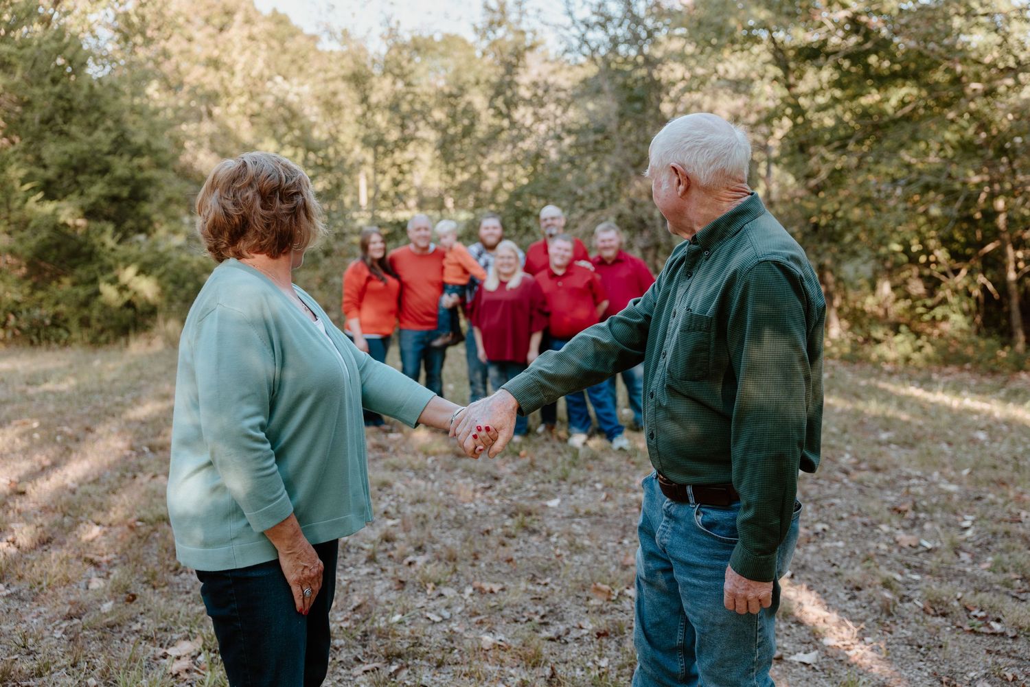 A couple in casual attire shares a tender moment on a wooded trail during an autumn day.