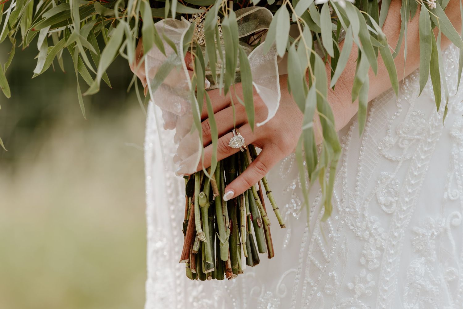 Close-up of bride holding eucalyptus bouquet with diamond ring, wearing lace wedding dress.