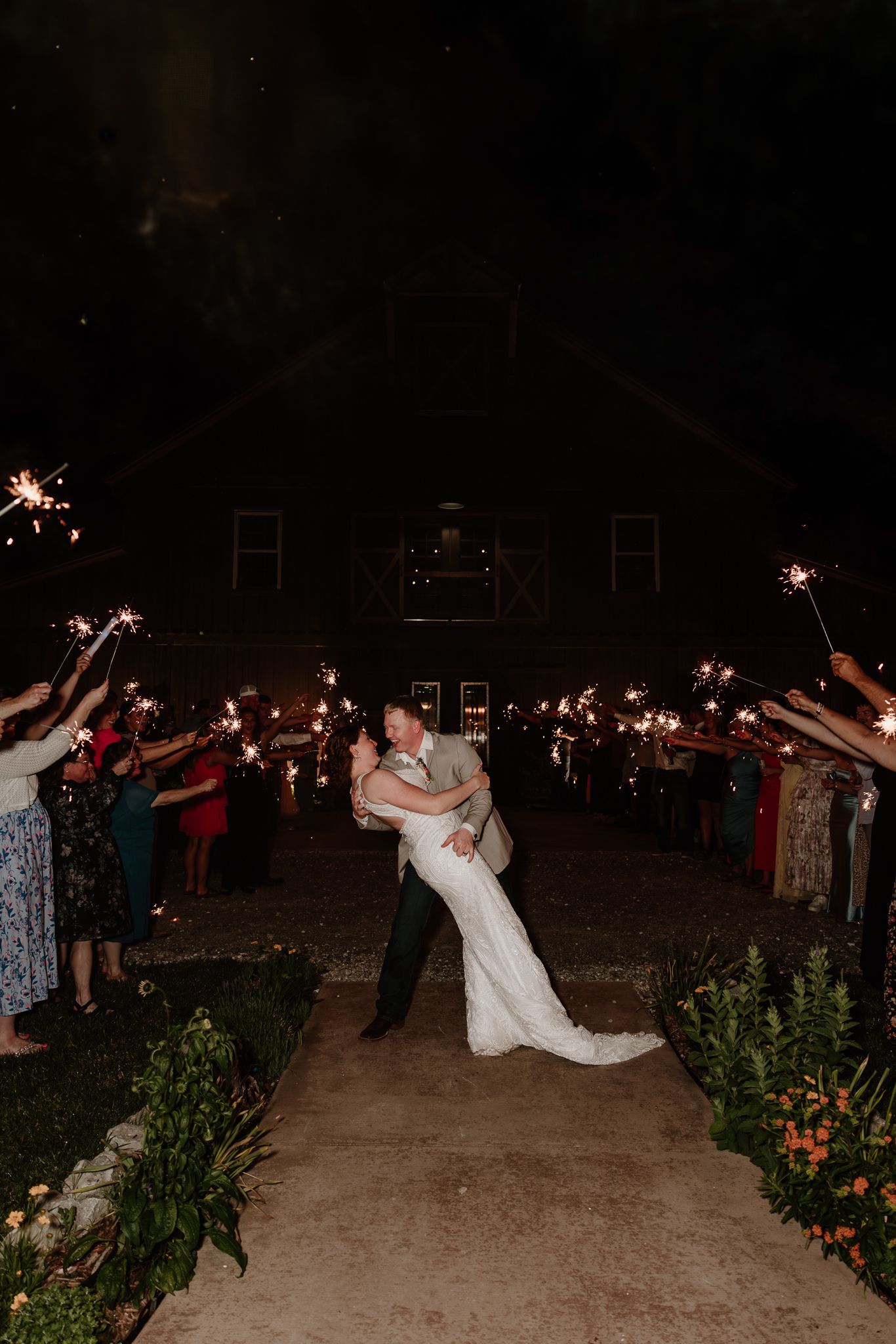 Bride and groom share a romantic dip kiss during a sparkler exit at their nighttime barn wedding reception.