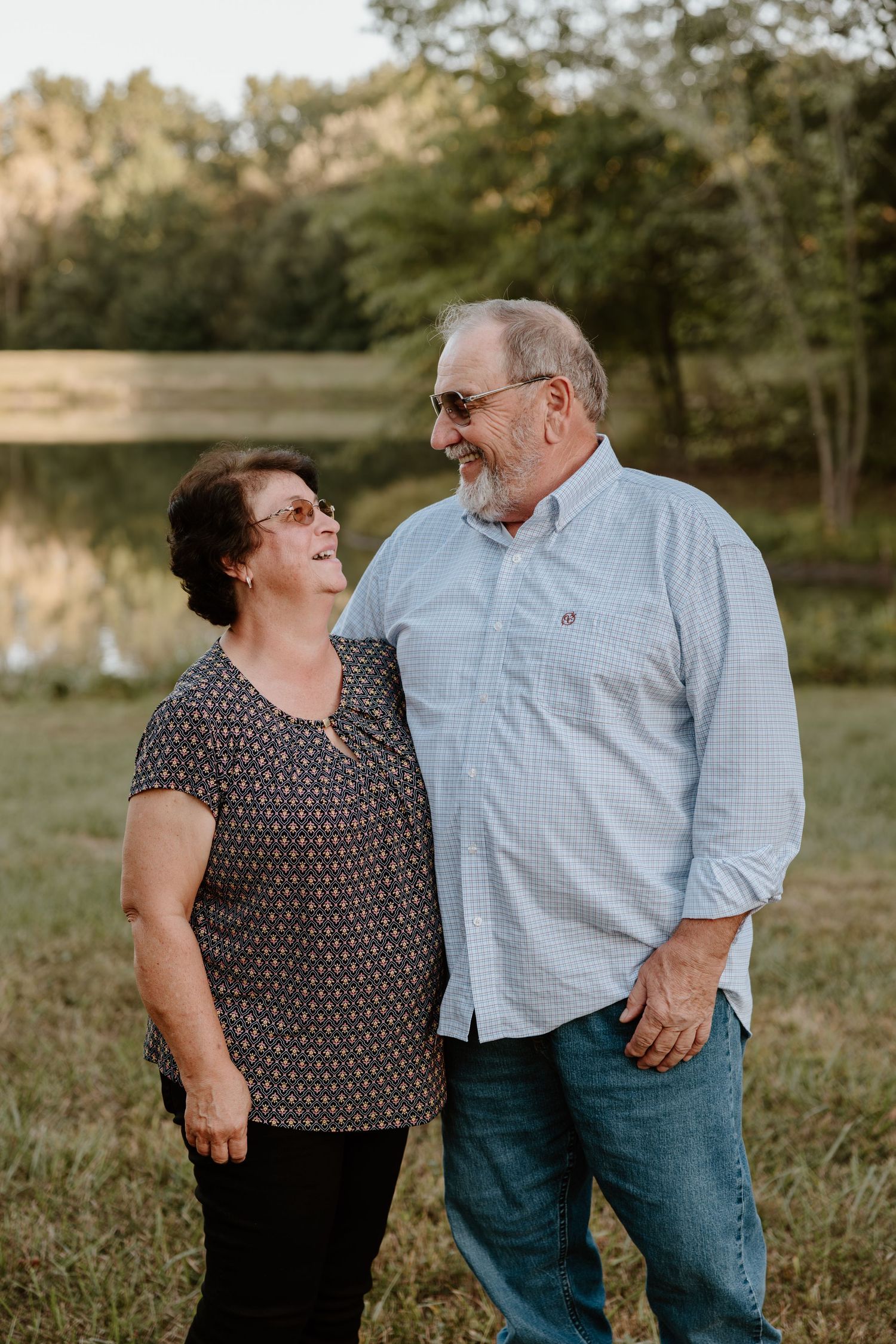 A couple shares a loving moment while standing together by a lake during golden hour.