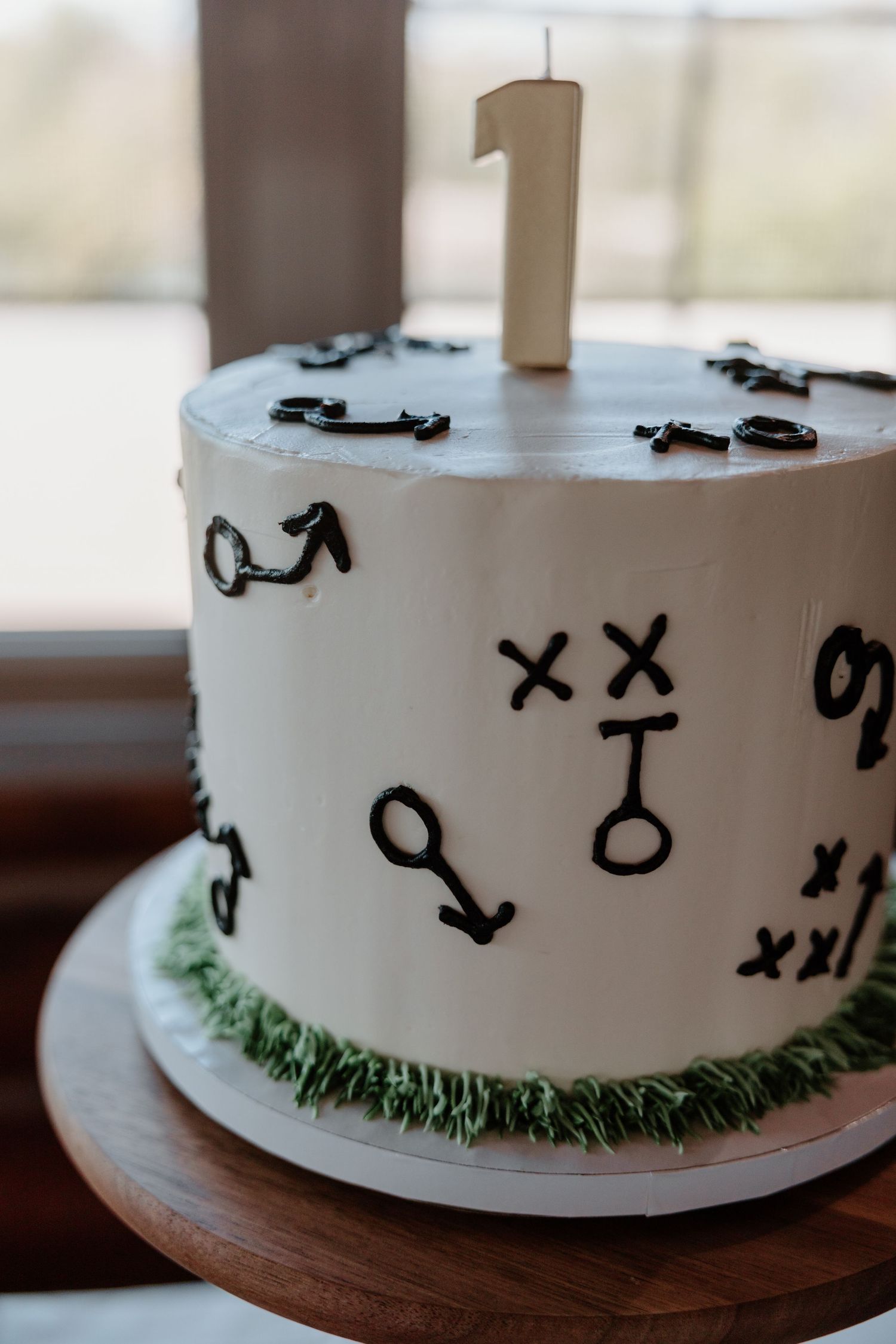 A white frosted cake decorated with black stick figure drawings and green grass piping around the base.