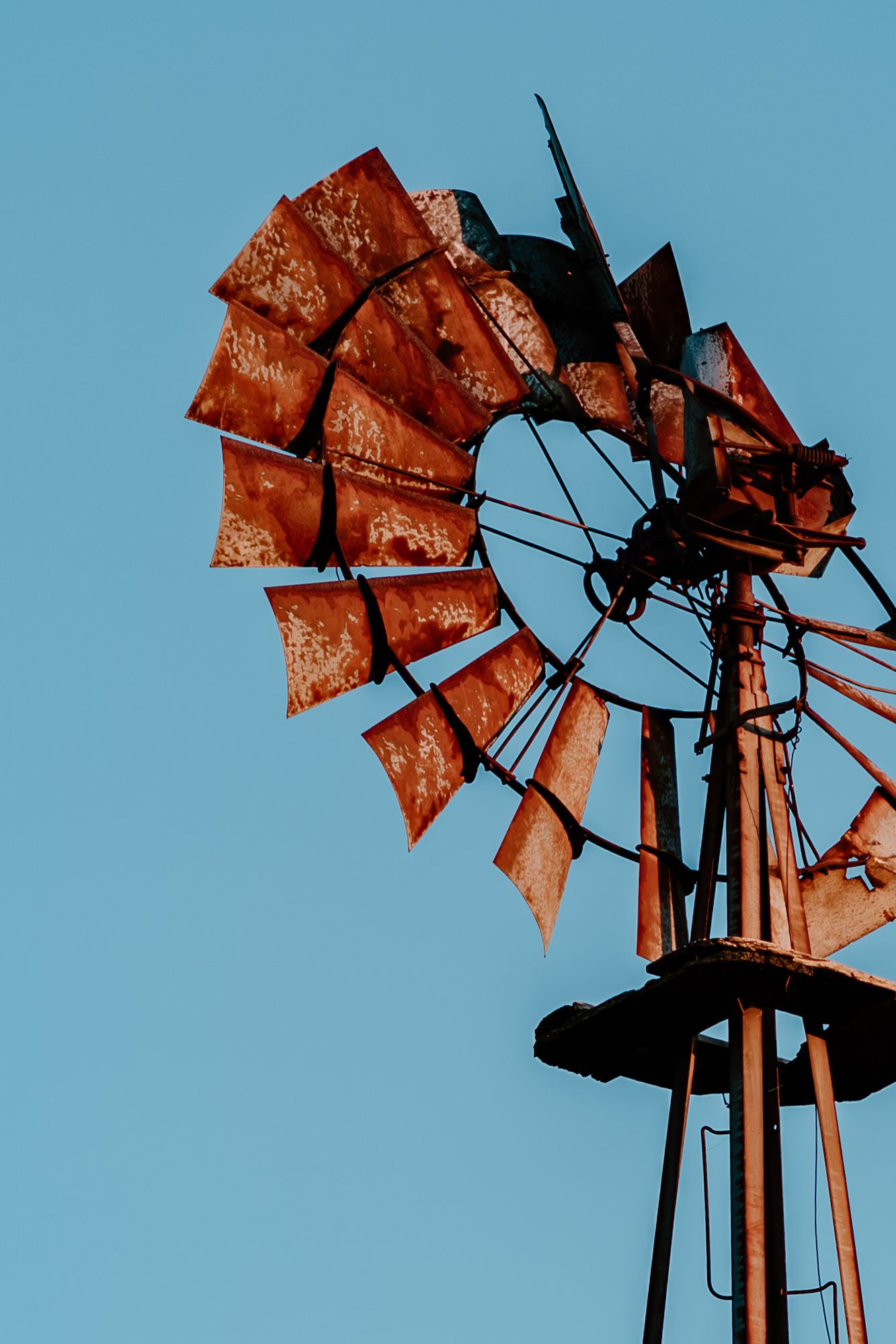 Silhouette of a rustic windmill with orange-tinted metal blades against a bright blue sky at sunset.