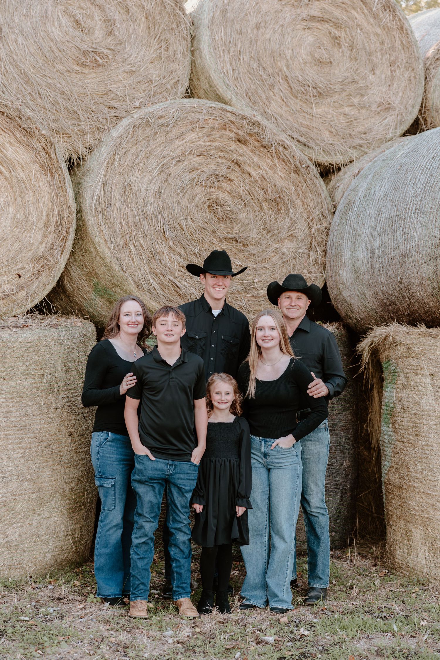 A family poses together in front of large round hay bales wearing coordinated black and blue outfits.