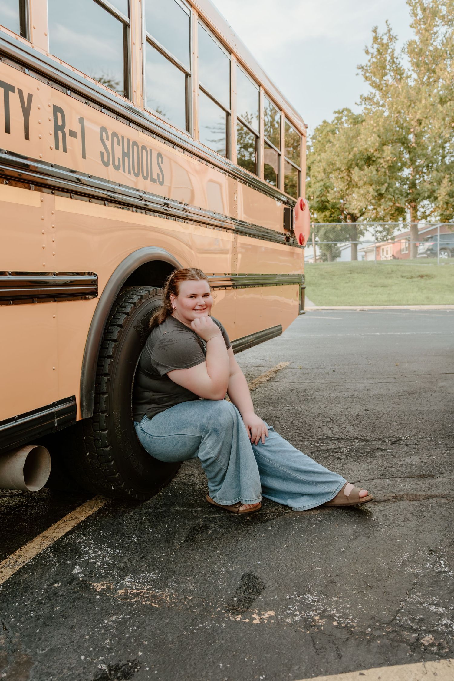 Student poses next to a large yellow school bus tire in a parking lot.