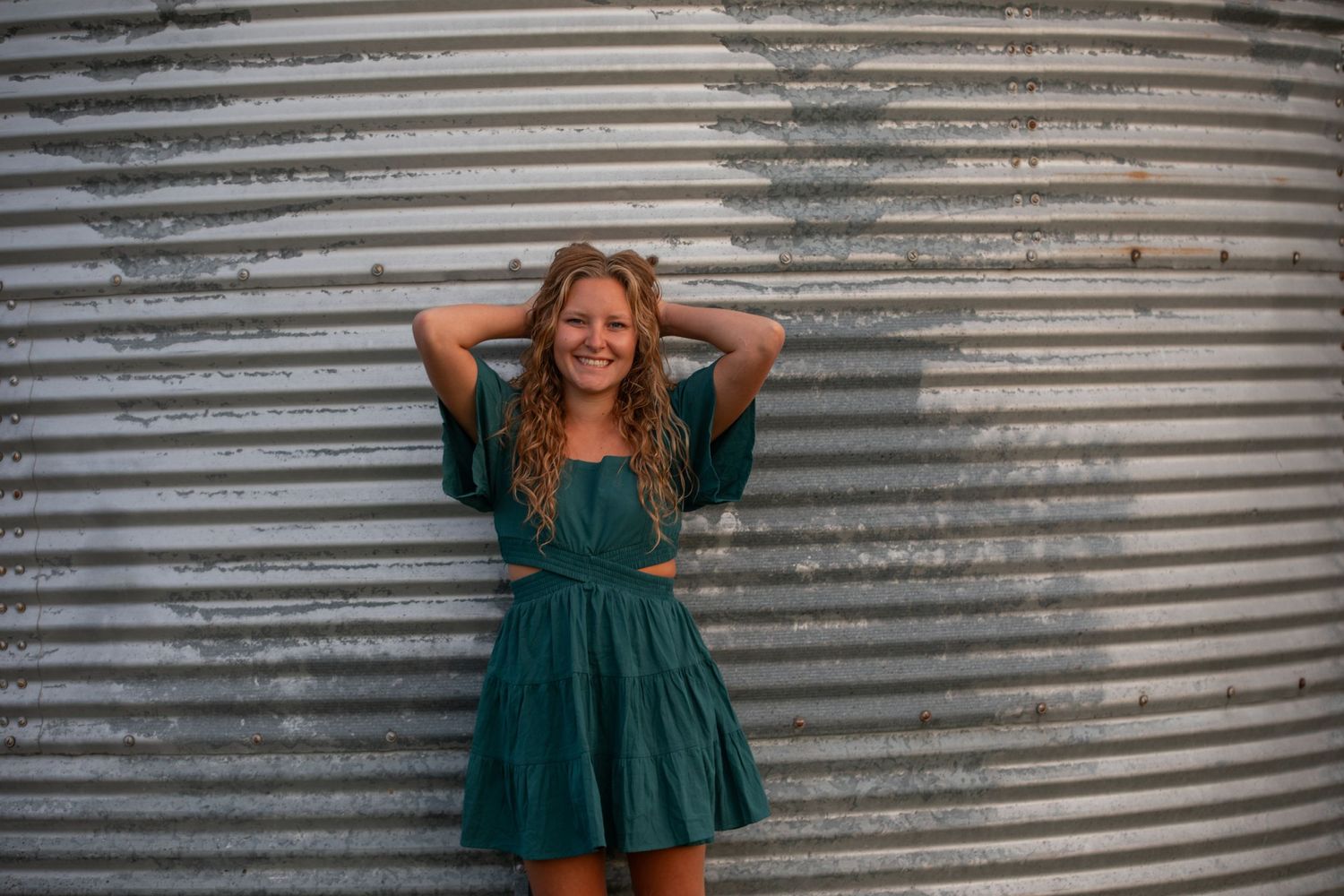 Person in green dress posing against corrugated metal wall.