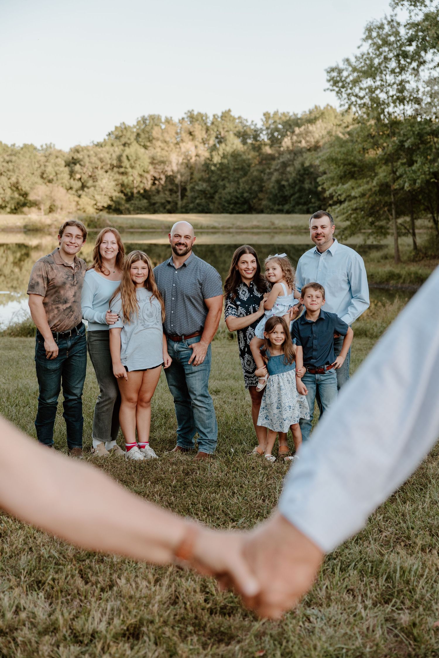 A group poses together in a grassy field at sunset wearing coordinated blue and white outfits for outdoor family photos.