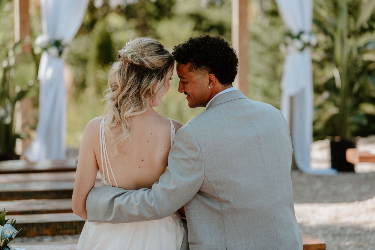 Bride and groom sharing an intimate moment from behind at an outdoor wedding ceremony with floral arch decor.