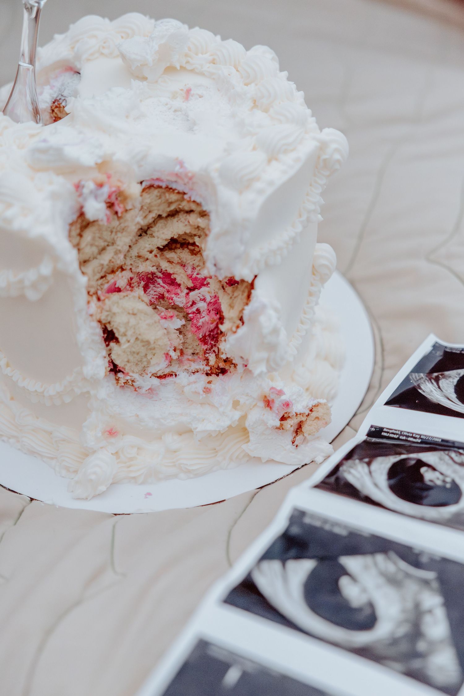 A white frosted cake with red filling sits beside black and white ultrasound photos on a light colored surface.