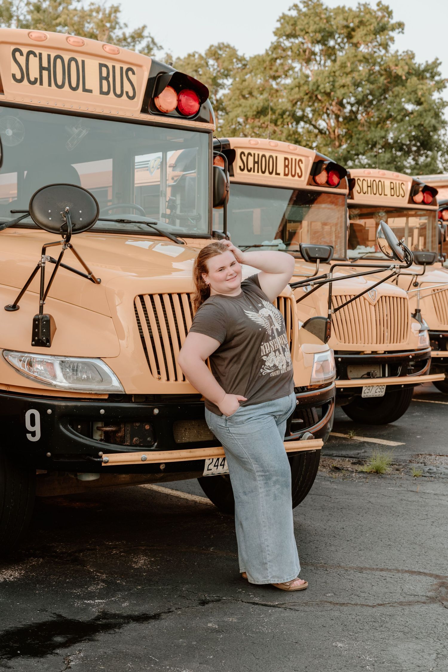 A row of three yellow school buses parked in a lot with someone posing in front.