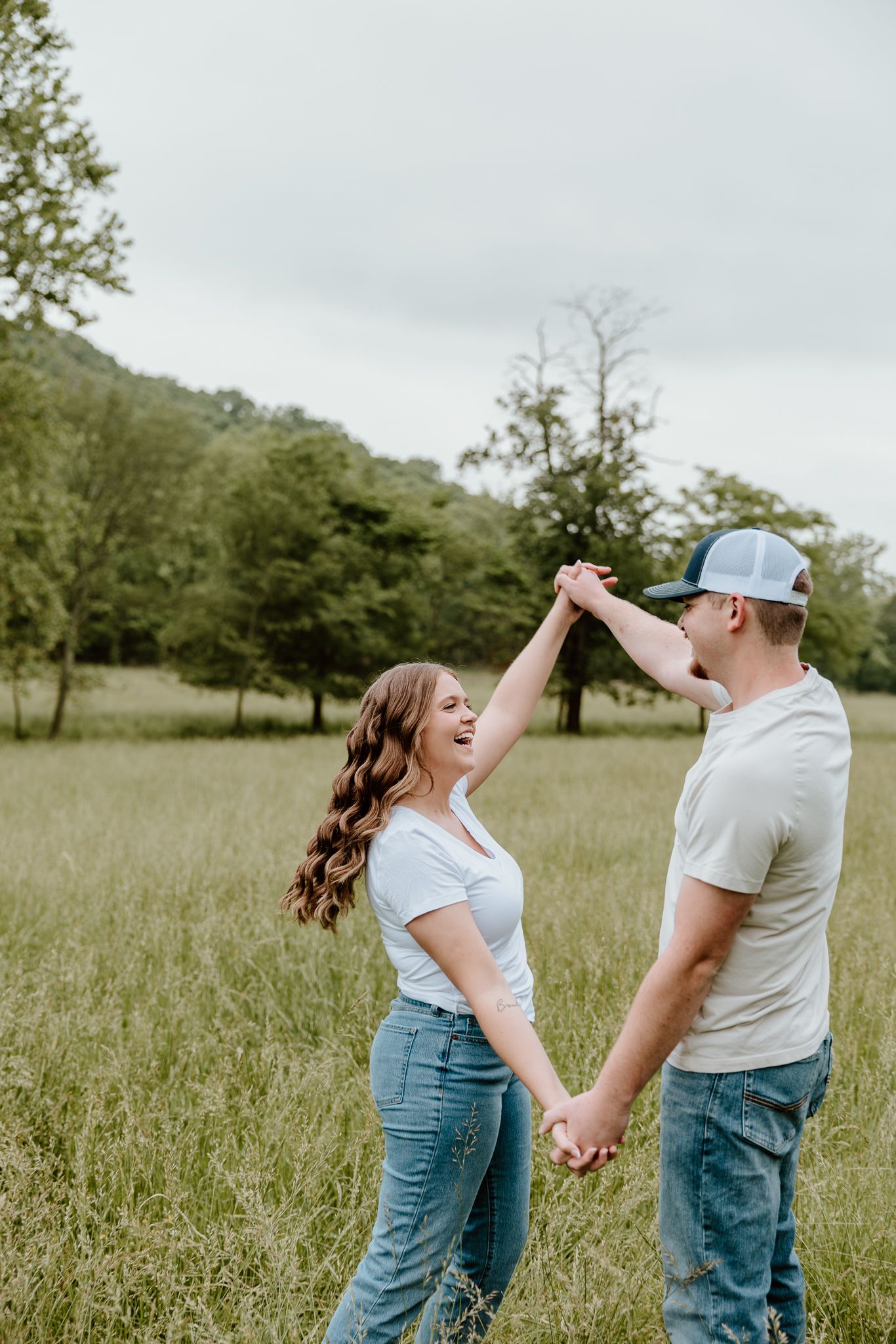 Happy couple dancing and holding hands in a lush green meadow, wearing white tees and jeans.