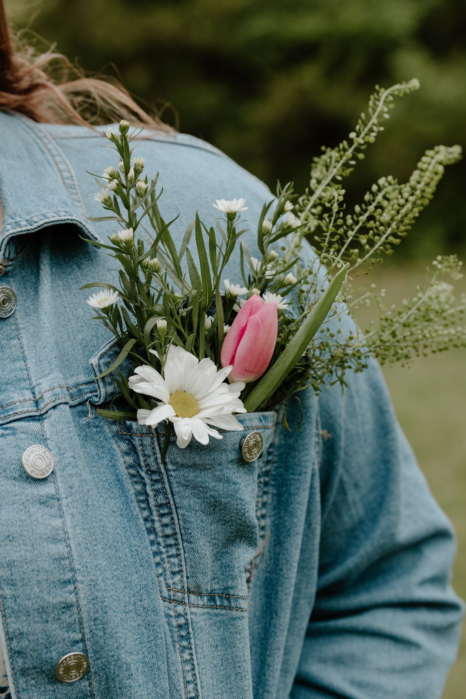 Fresh spring flowers including a pink tulip and white daisy tucked into the pocket of a light denim jacket.