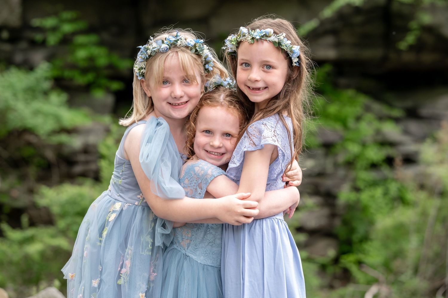 wedding portrait of three little flower girls in pale blue dresses with blue flower crowns hugging and smiling for a photo