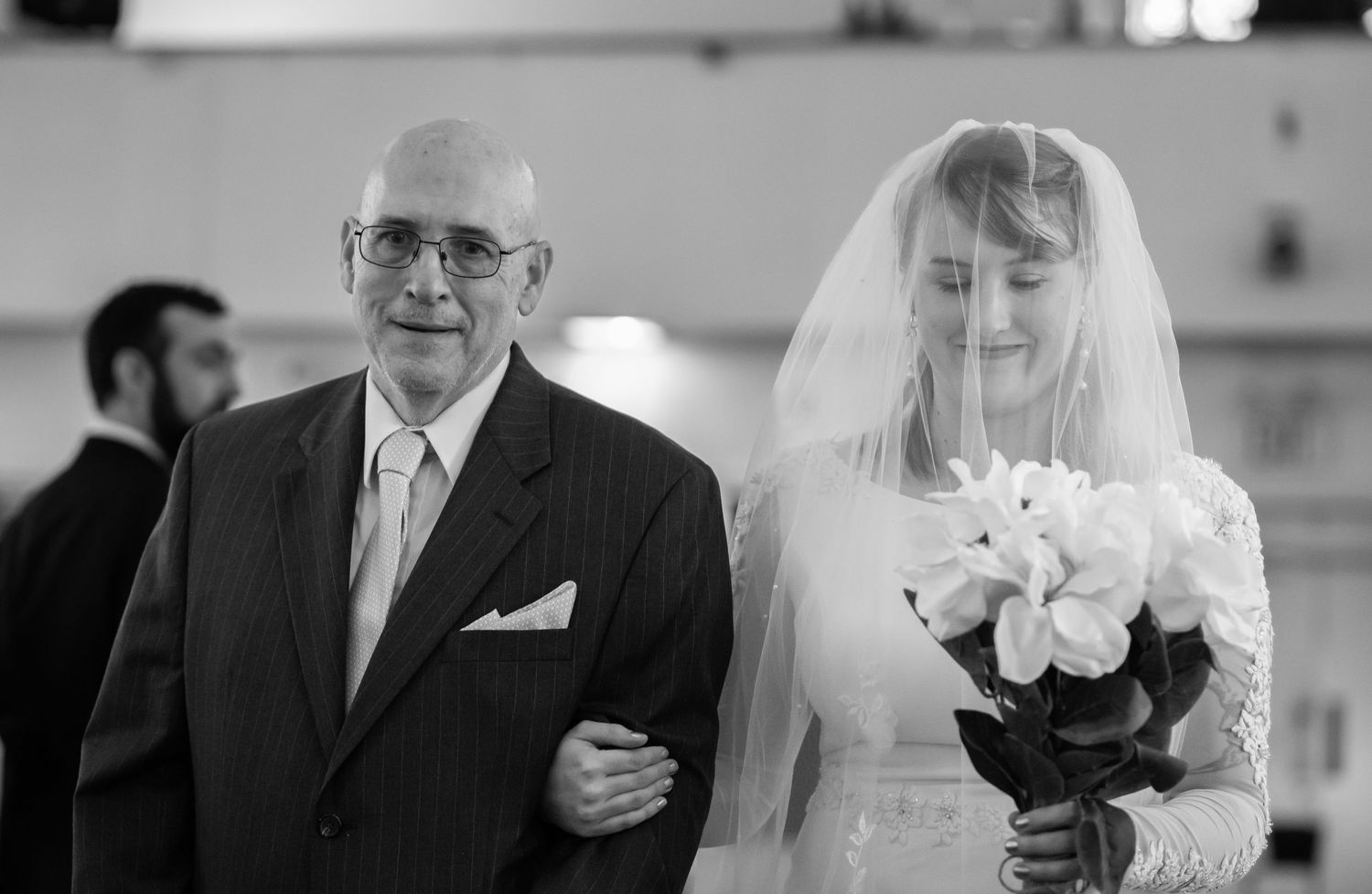 a veiled Catholic bride walks down the aisle arm in arm with her father