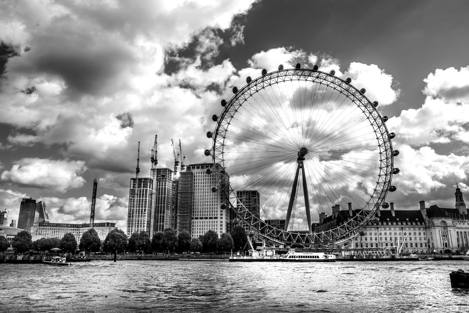 Black and white photo of the London Eye Ferris wheel on the River Thames with dramatic cloudy sky.
