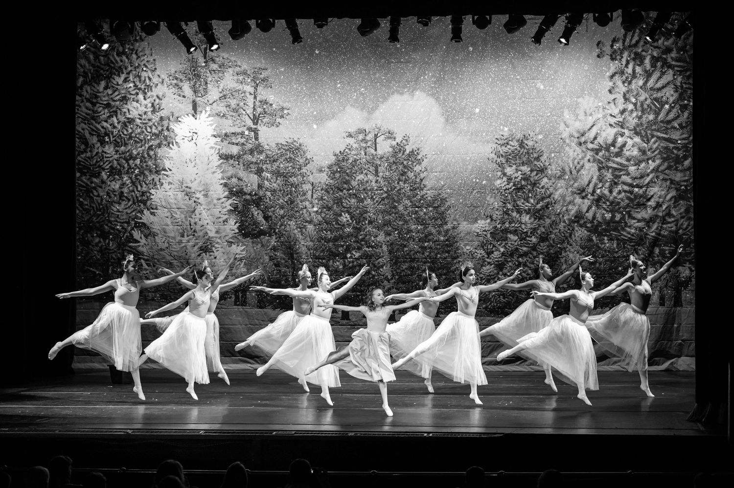 black and white of a ballet performance on stage, with multiple dancers in white tutus and a winter scene in the background