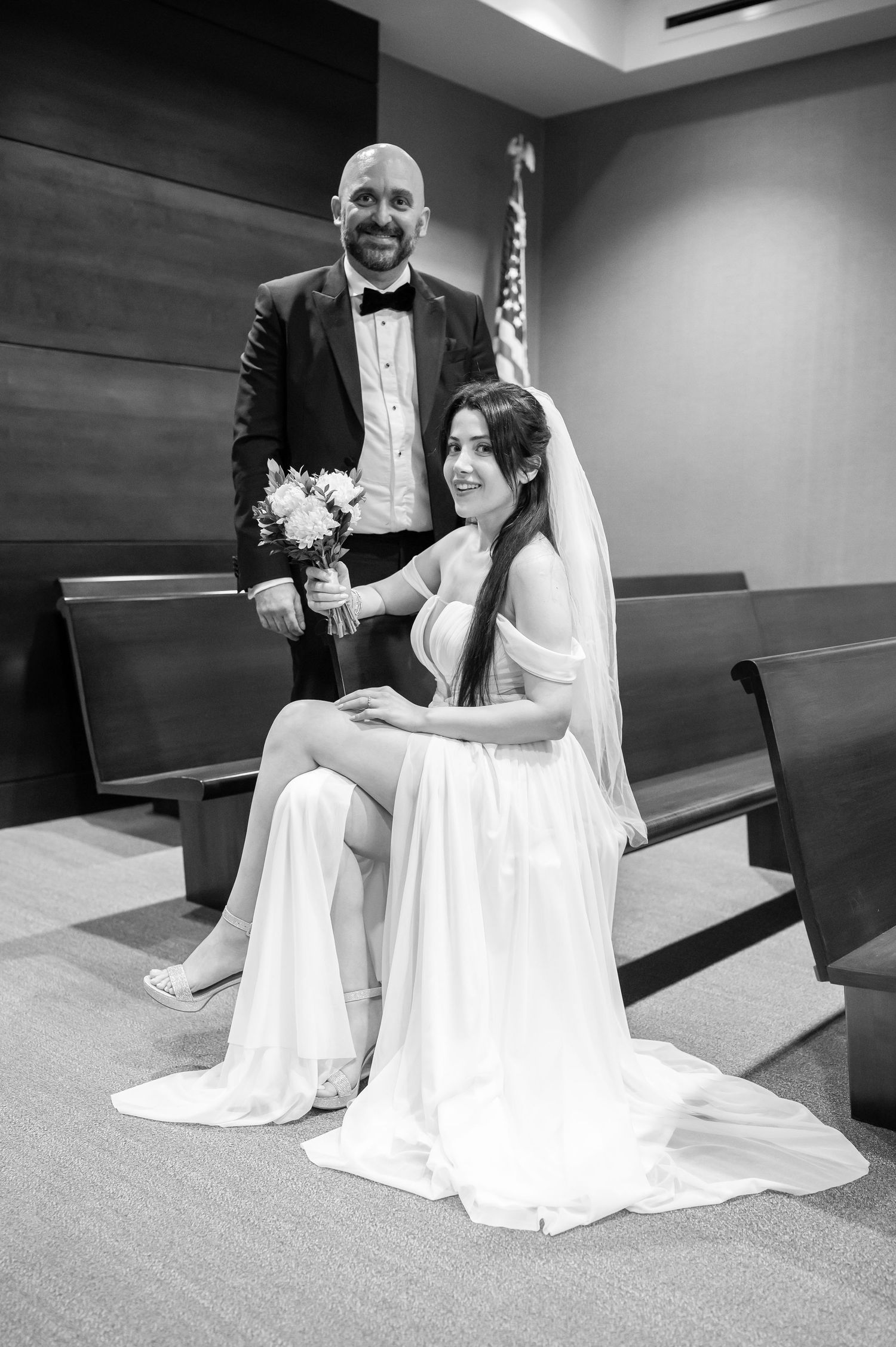 a bride and groom pose for a portrait in front of a large American flag in a courthouse in Morgantown, WV