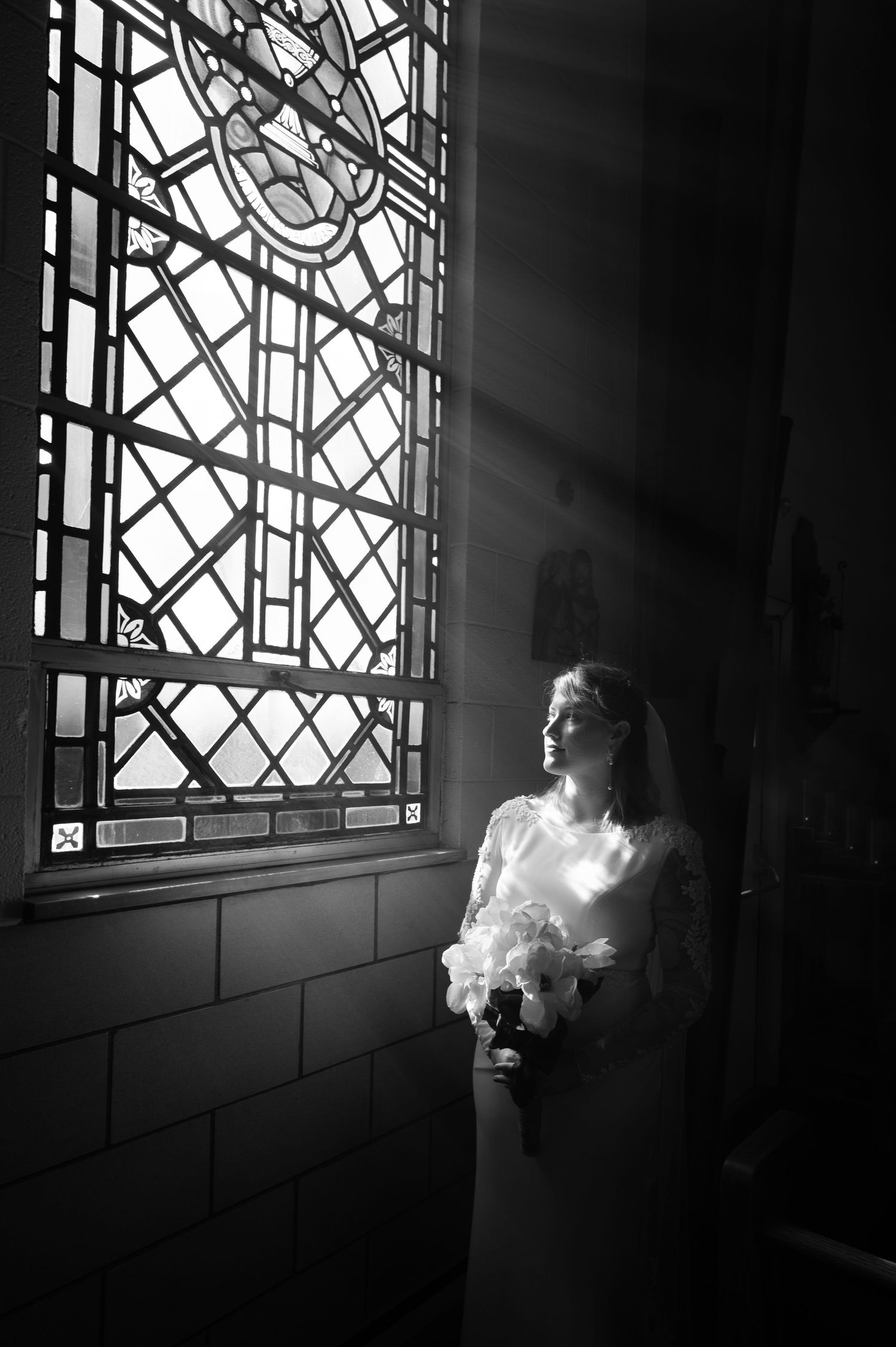 dramatic black and white portrait of a bride emerging from the darkness and illuminated by the light of an elaborate stained glass window