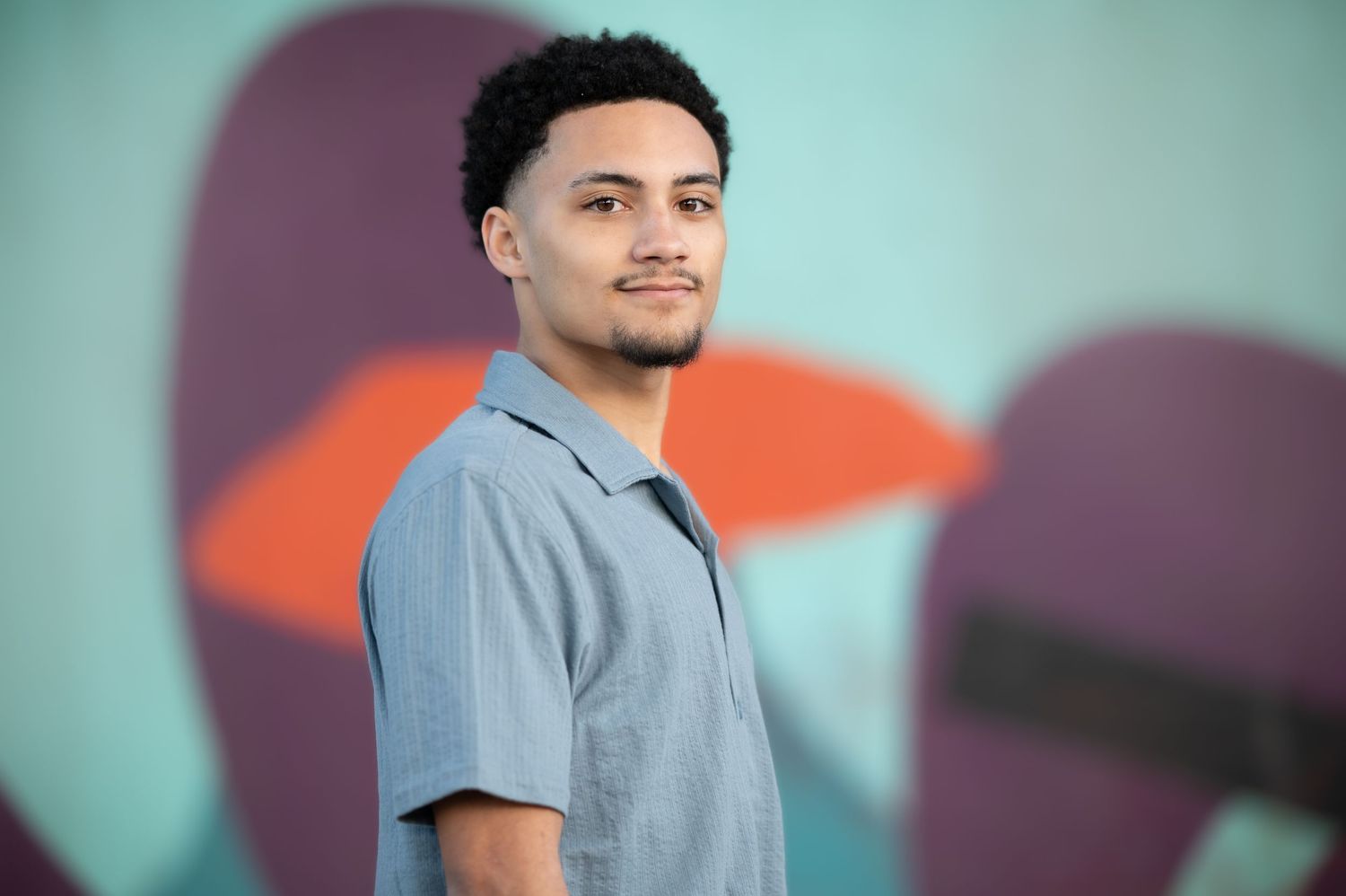 a young high school senior in a blue shirt poses with a large colorful mural in the background
