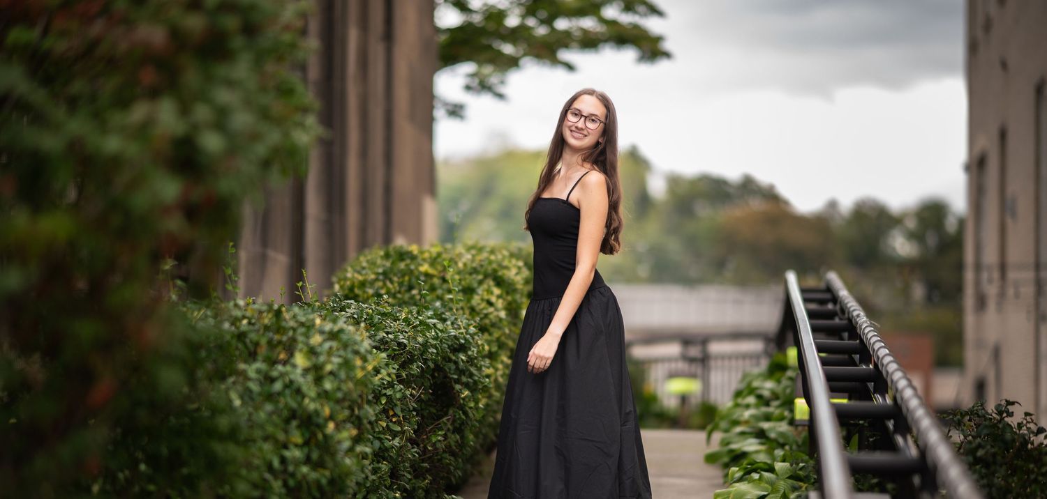 a senior student in a long black dress poses outside a historic building on High Street in downtown Morgantown, WV