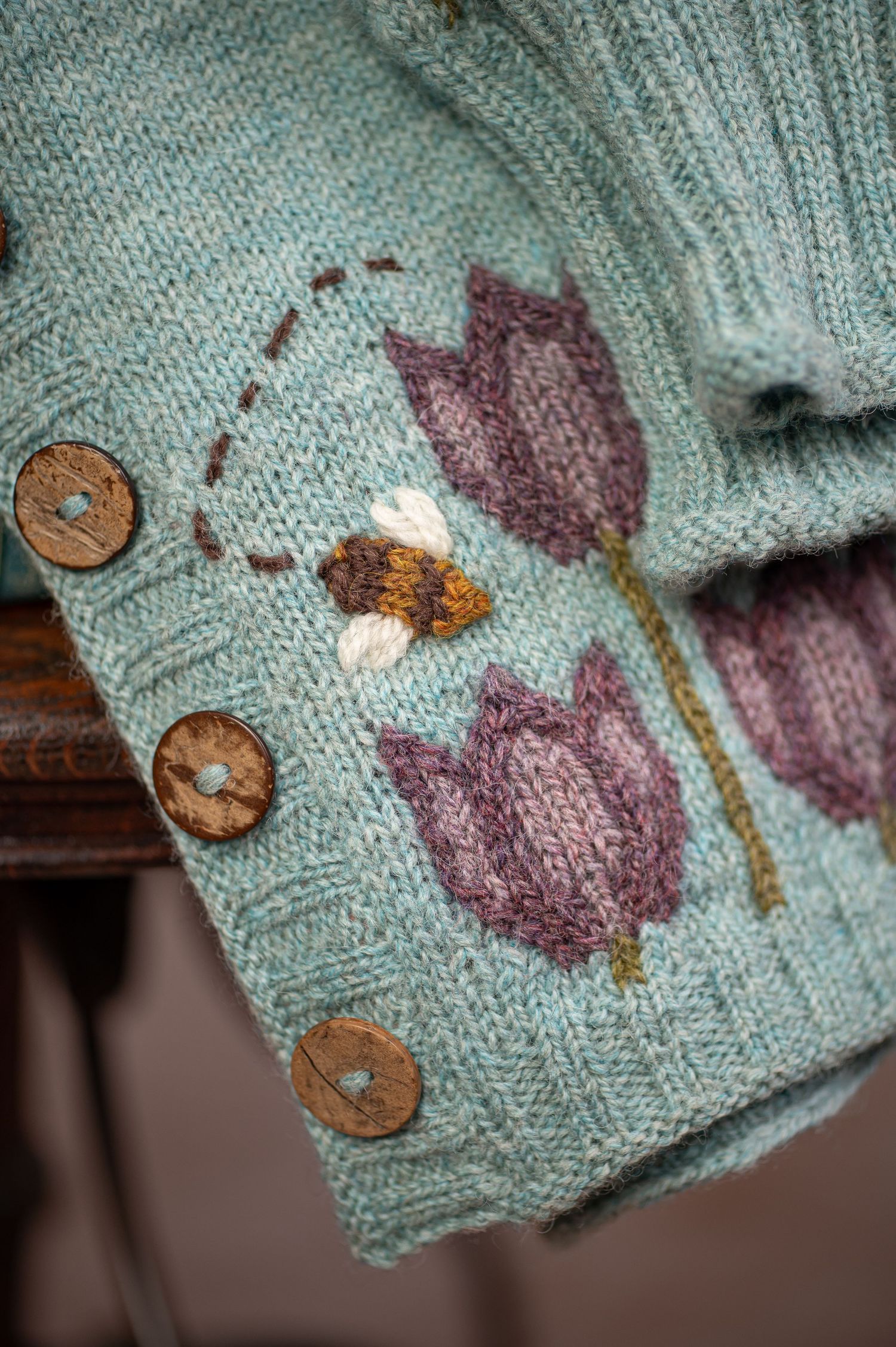 a closeup/macro shot of a hand knit sweater with an intricate tulip design and a little knit bumblebee