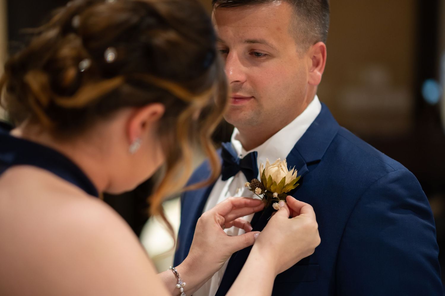 closeup candid shot of a bridesmaid carefully pinning a boutonnière onto a groomsman's jacket