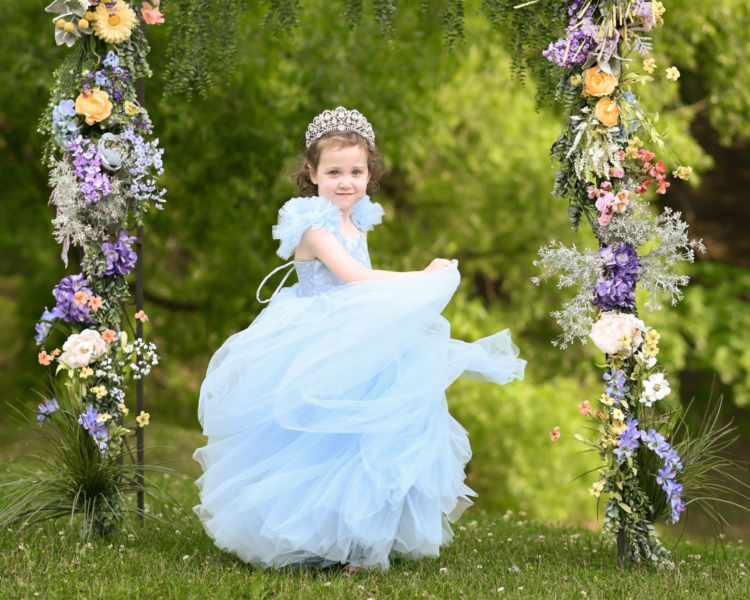 spring floral portrait of a little girl in a long fluffy blue dress under a flower covered arch